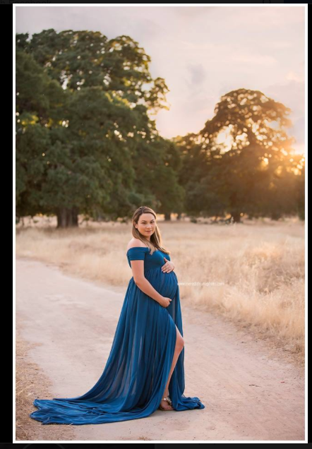 A person in a flowing royal blue dress poses gracefully on a dirt path at sunset with golden light filtering through trees.