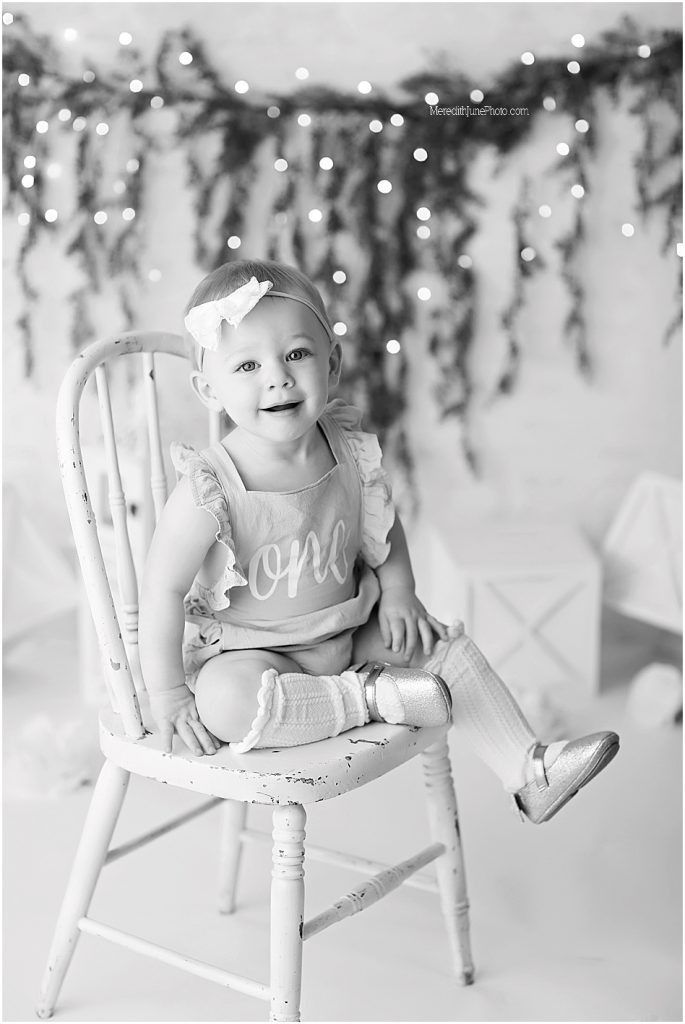 A series of black and white photos showing a small child sitting in a white wooden chair with twinkling lights in background.