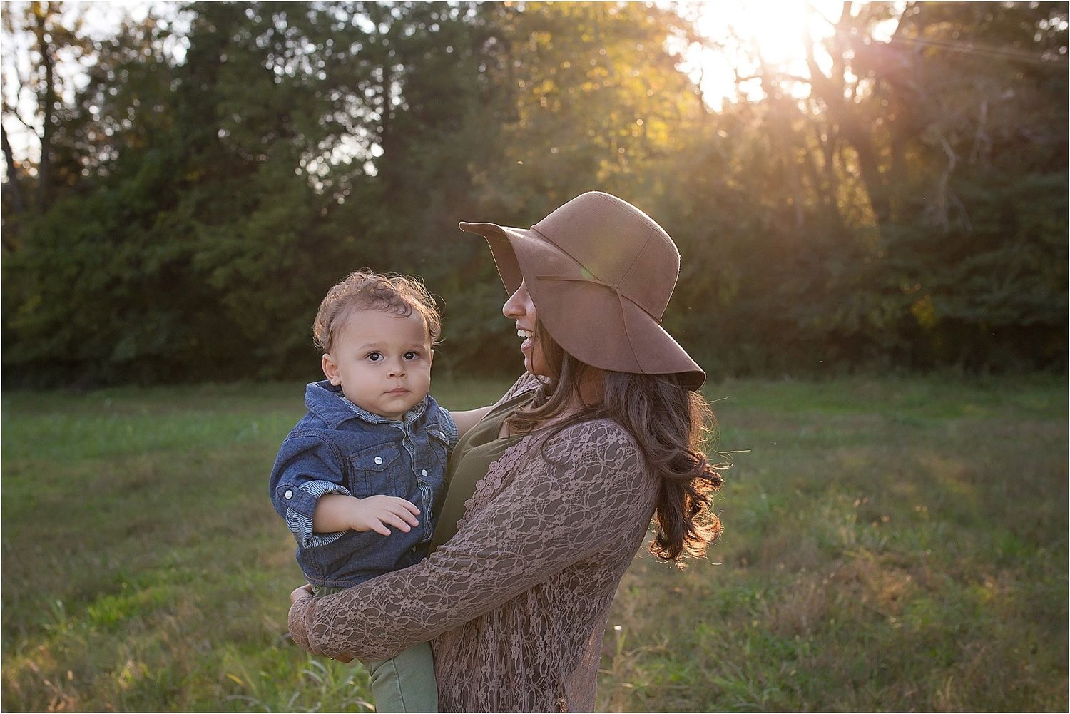 A candid family moment photographed in a field at sunset with warm golden light filtering through trees.