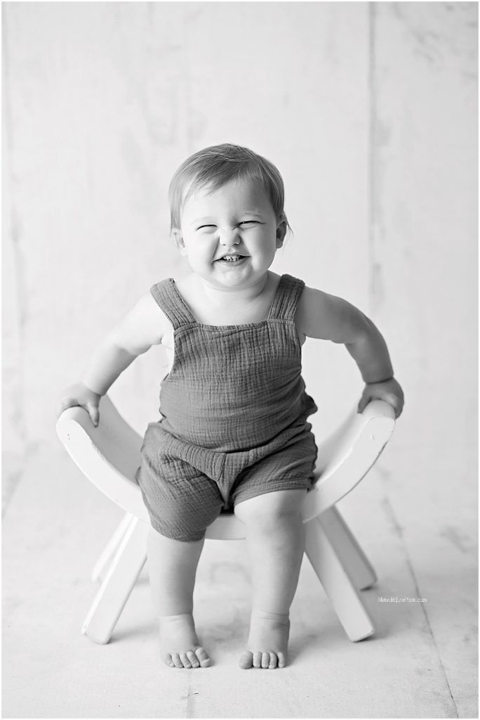 Black and white photo series showing a baby in overalls sitting and playing on a white floor.