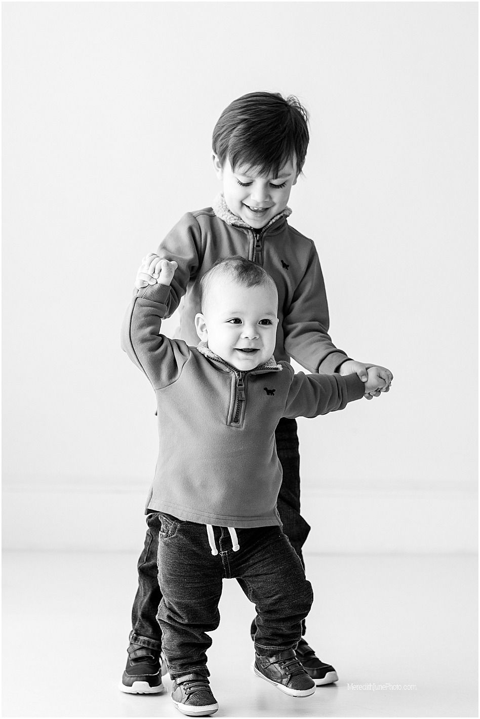 Black and white photo series showing a small child learning to walk and stand in casual clothing.