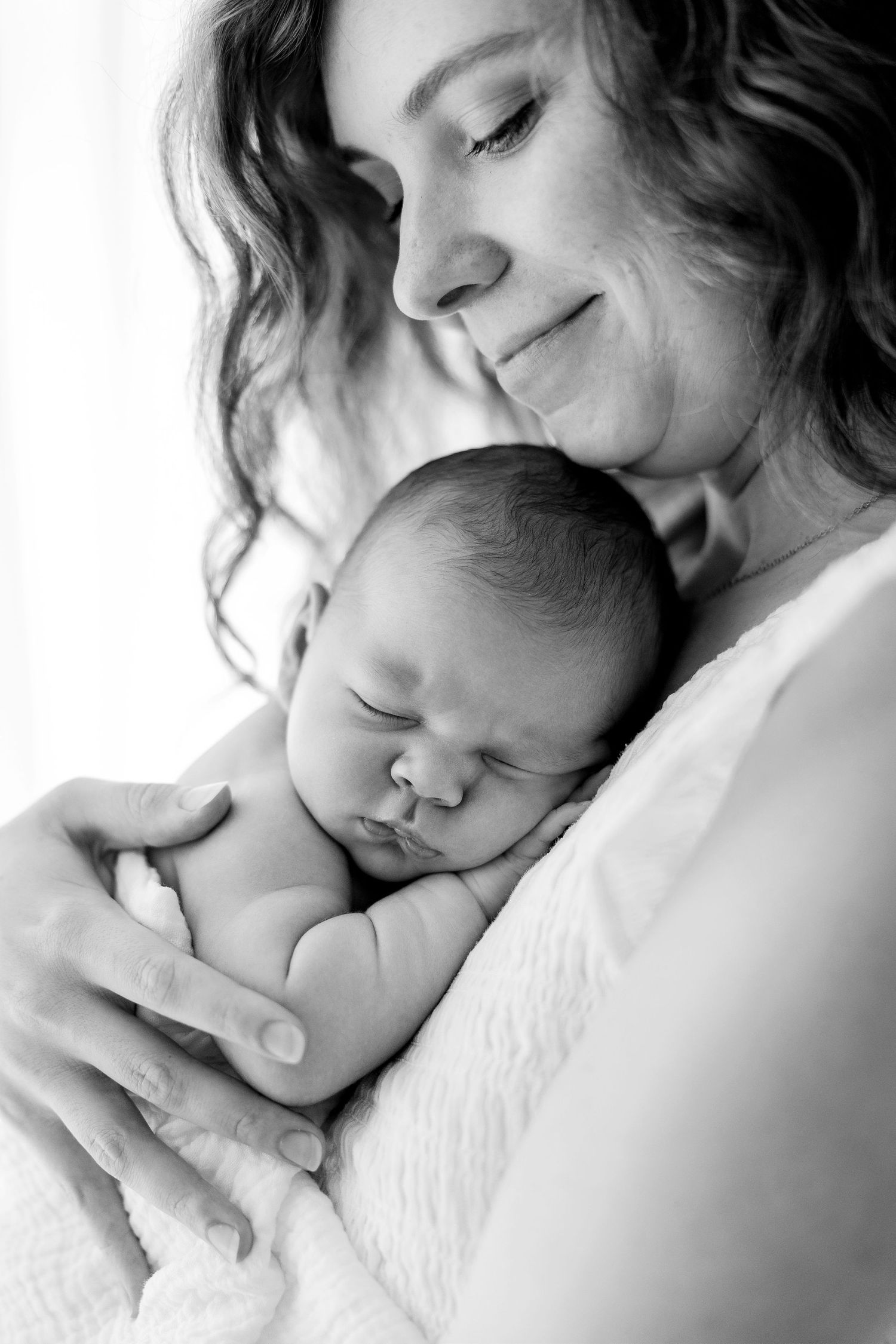 Black and white photo of a smiling mother tenderly cradling her sleeping newborn baby close to her chest.