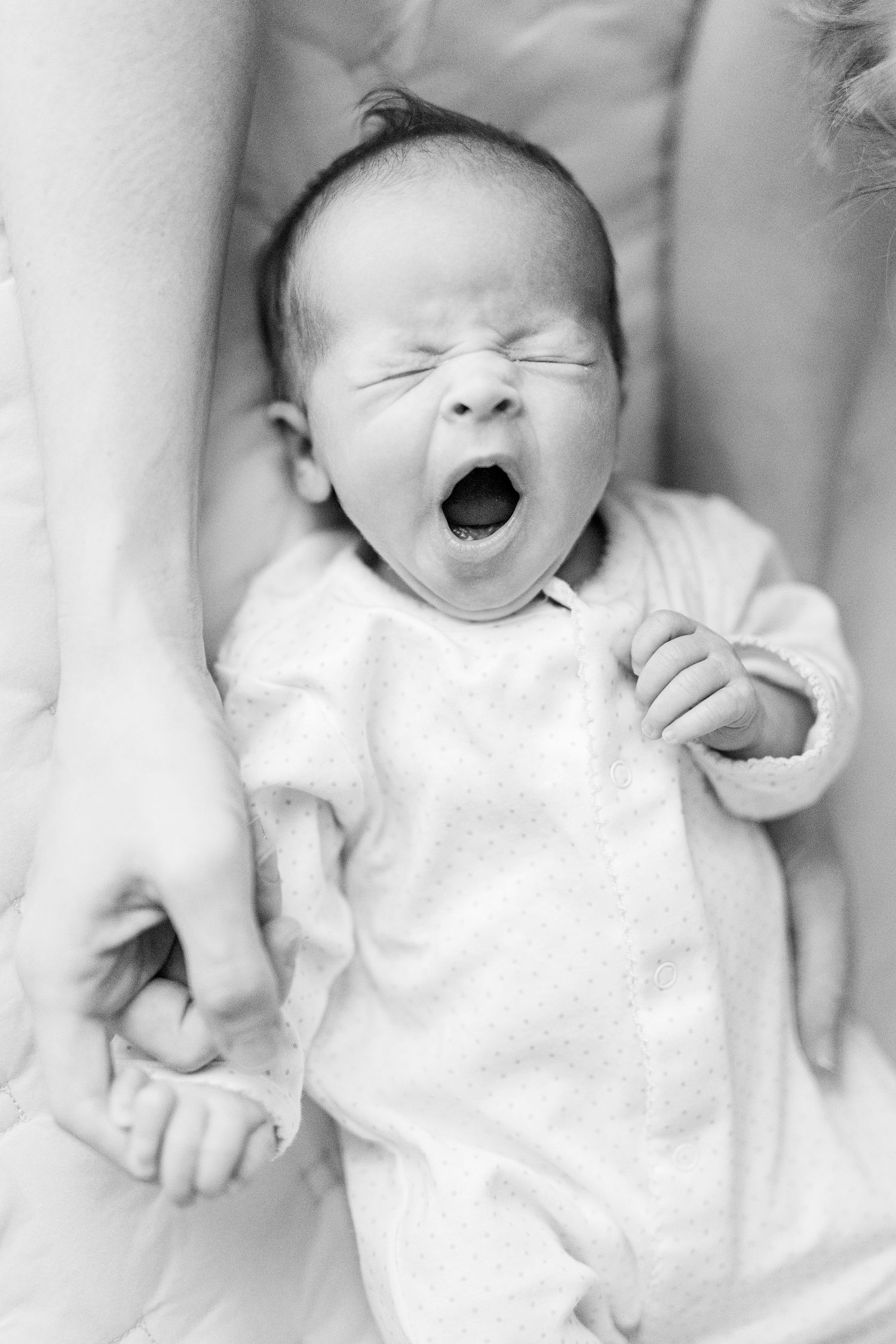 Black and white photo series showing a baby yawning and making adorable expressions while wearing white clothing.