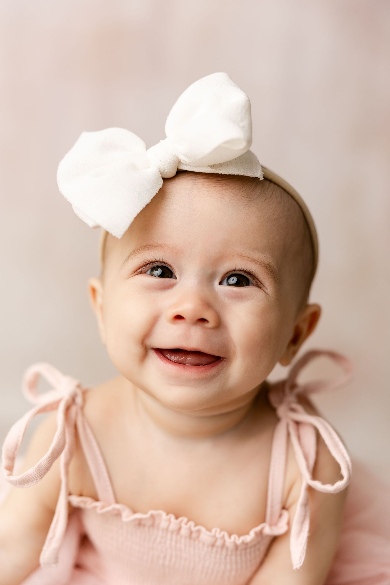 Baby in pink outfit with white bow headband smiling during portrait session.
