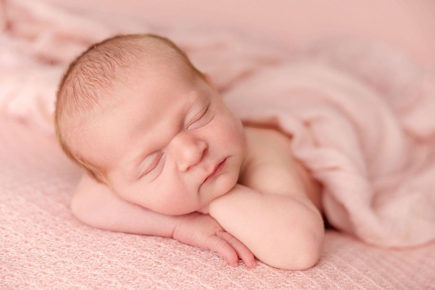 Sleeping newborn baby wrapped in soft pink blankets in a peaceful pose during professional photoshoot.