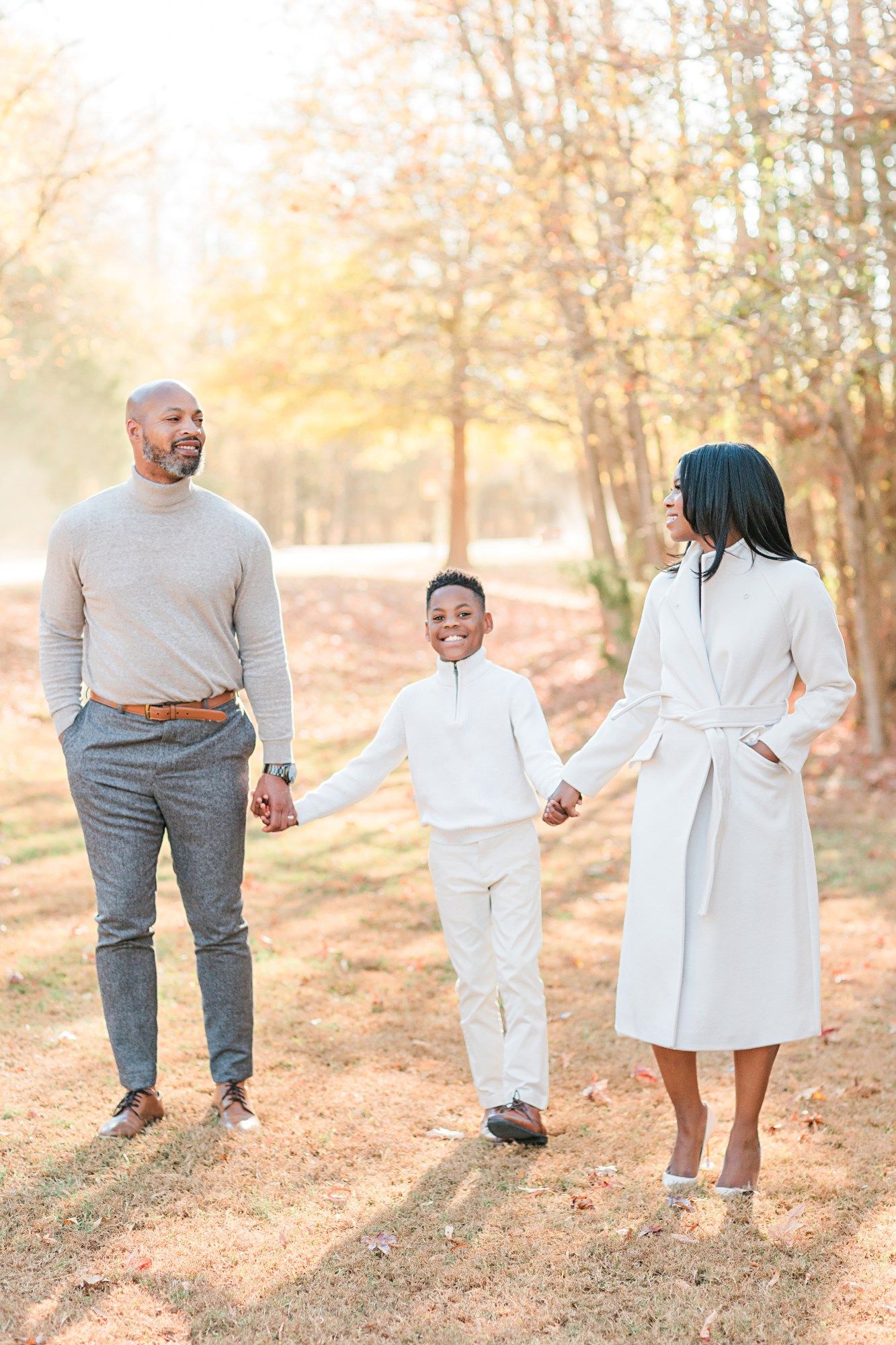 Family in white outfits walking together in sunlit autumn forest.