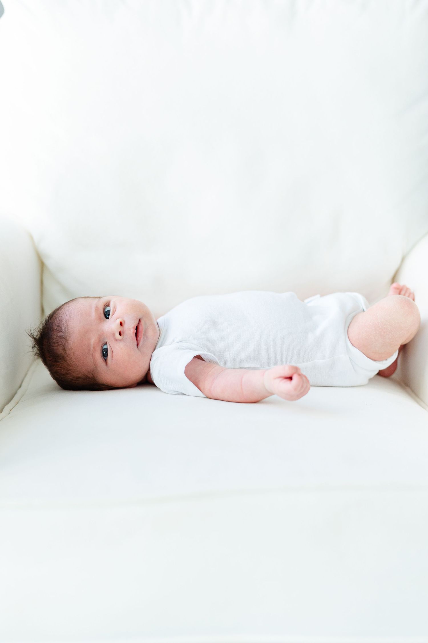 Baby in white onesie lying on white background captured in minimalist panoramic style shots.