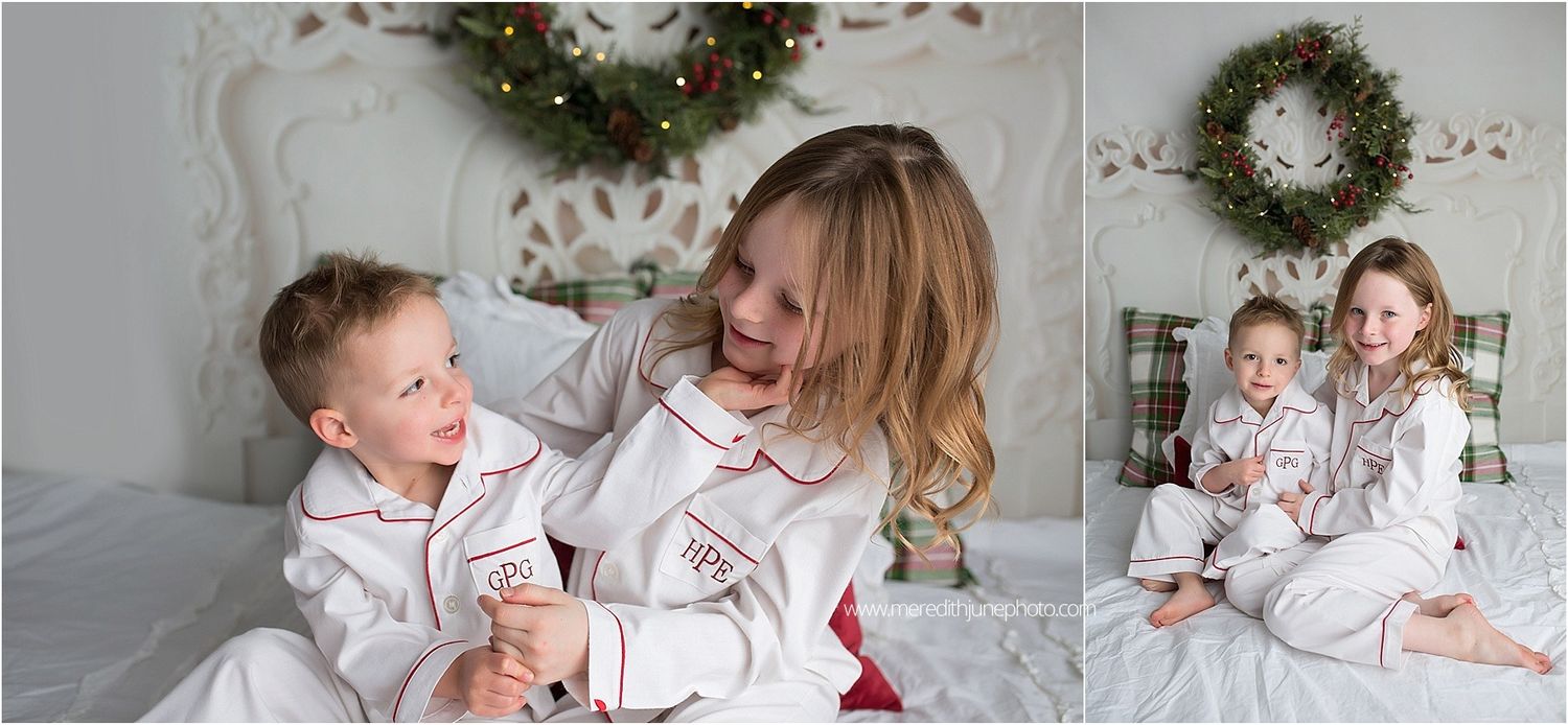 Cozy Christmas photoshoot with matching white and red outfits on plaid bedding with wreaths in background.