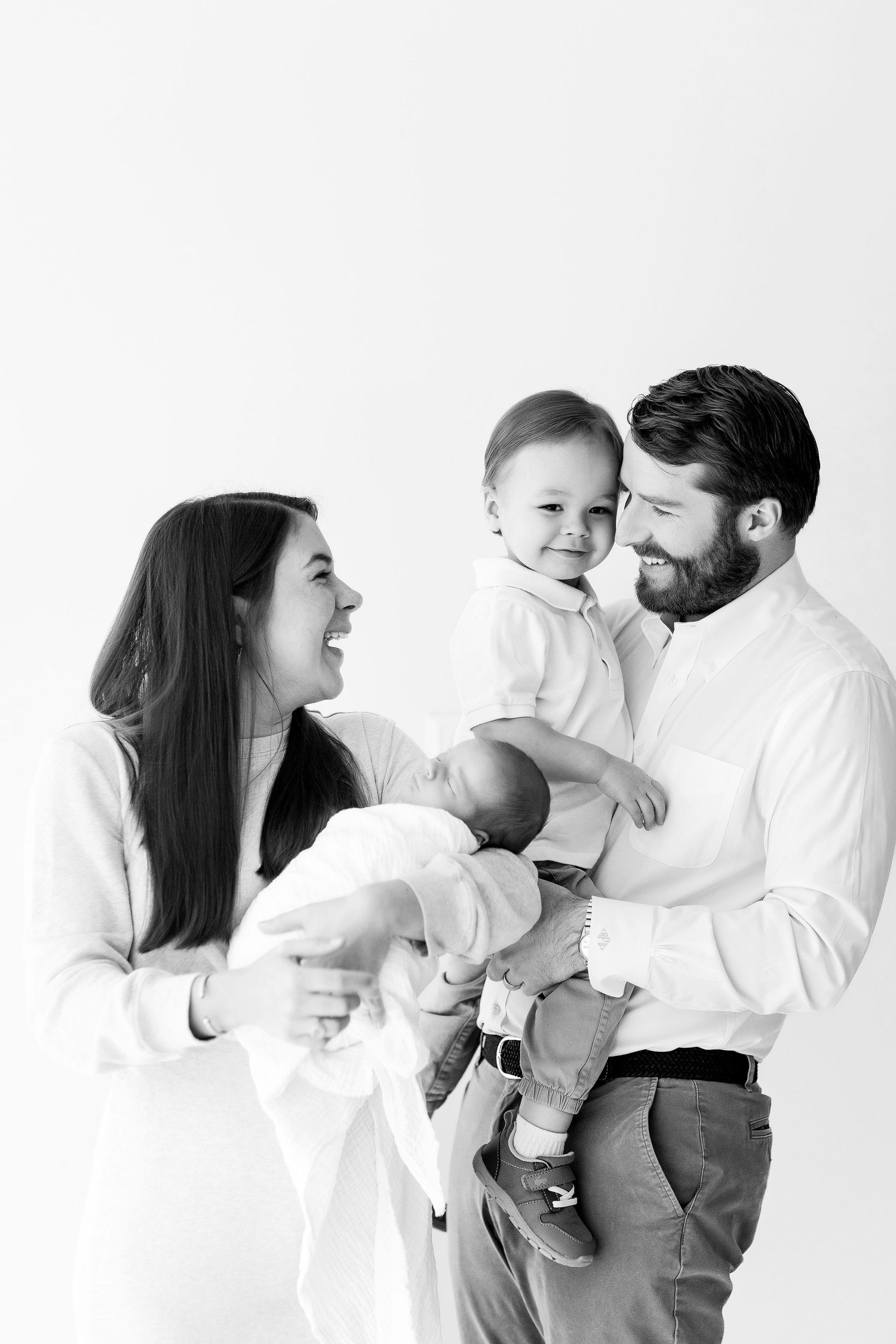 Family in white clothing shares joyful moments together against minimalist white background.