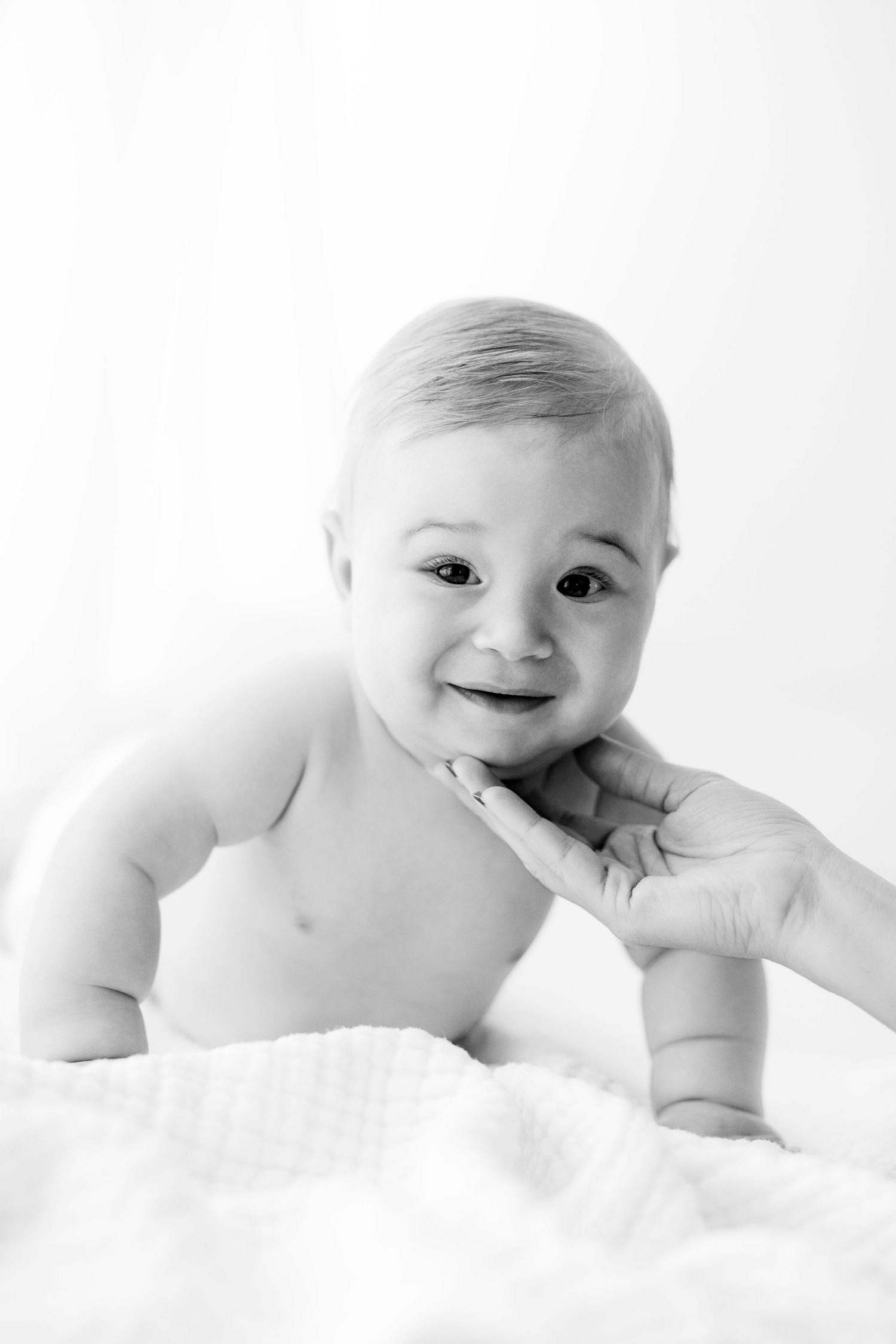 Series of black and white photos showing a smiling baby lying on white bedding.