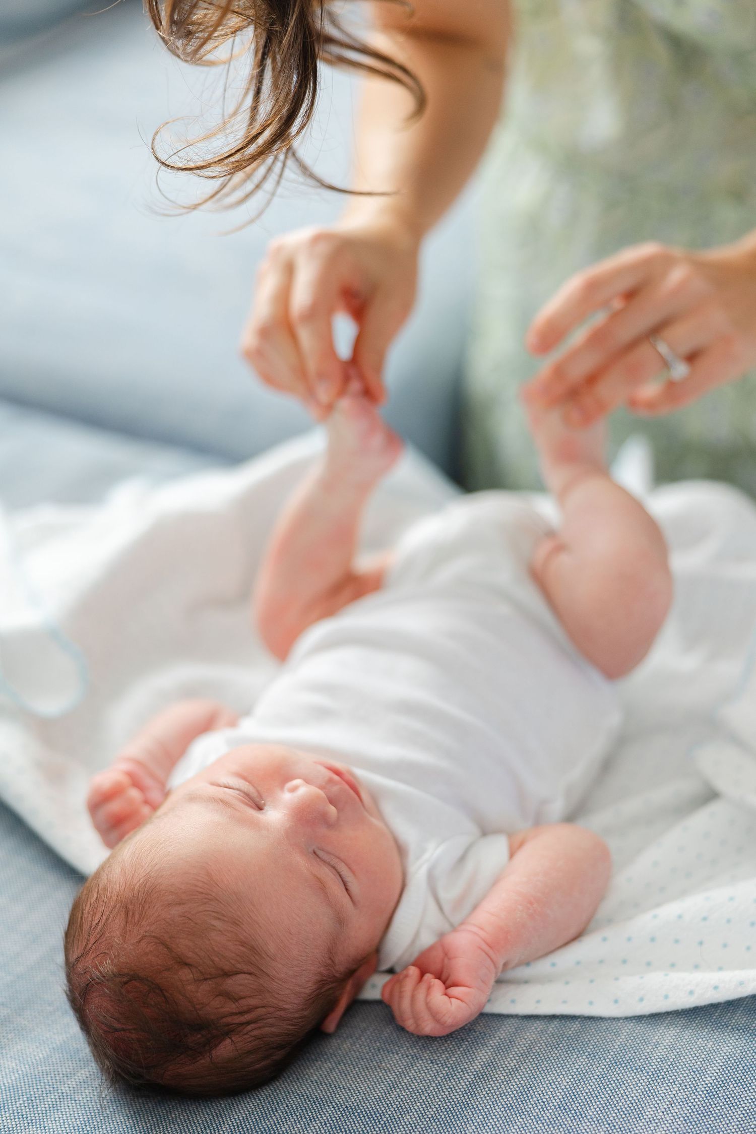 Gentle hands care for a sleeping newborn baby on soft white bedding.