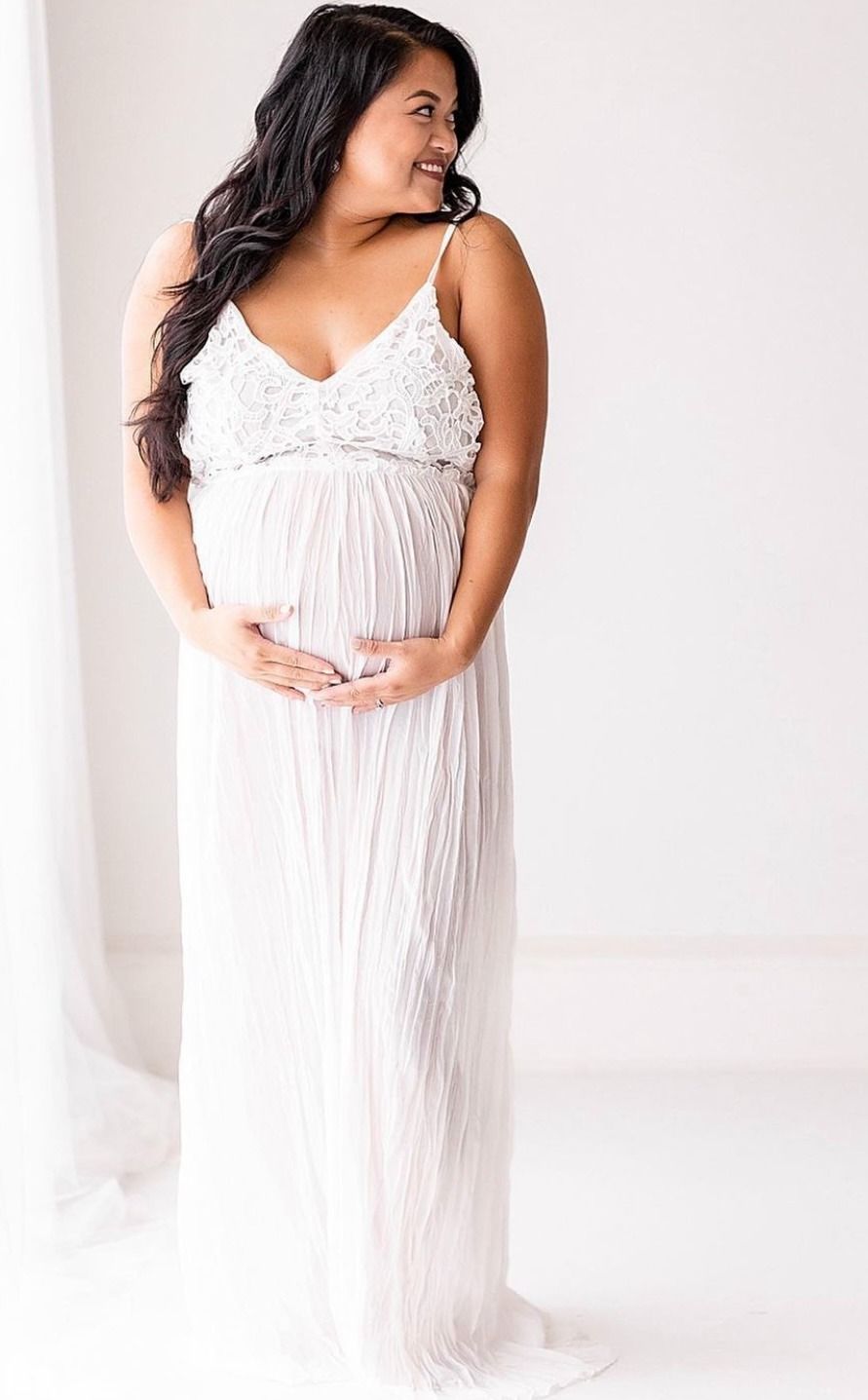 Woman in flowy white nightgown poses gracefully against light background in romantic boudoir photoshoot.