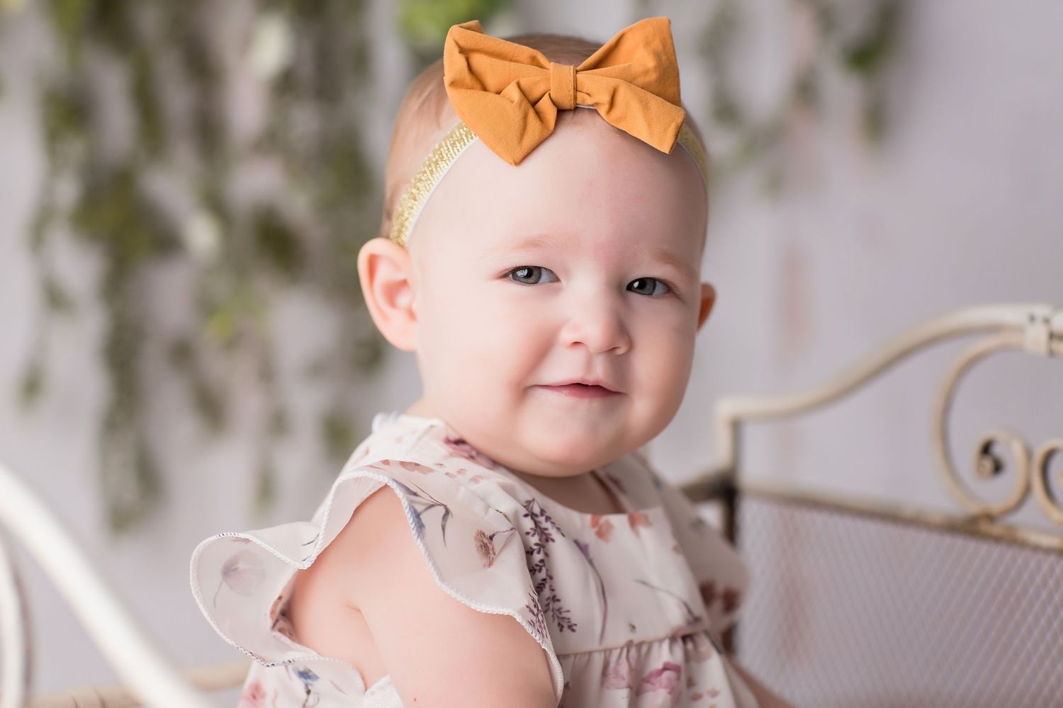 A small child wearing a ruffled dress and orange bow sits for a portrait with a dreamy background.