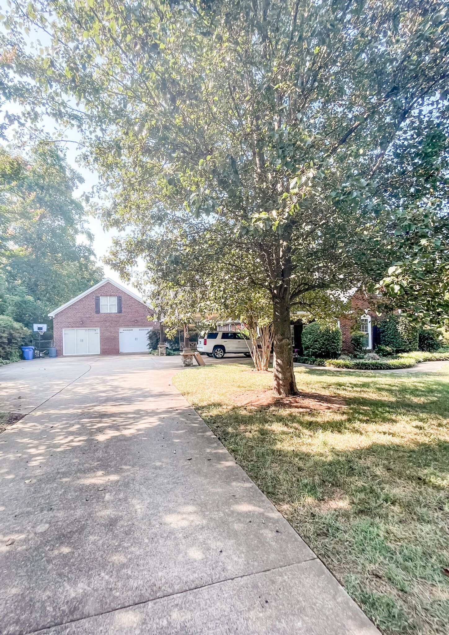 Long gravel driveway leading to a red brick garage with trees and landscaping on both sides.