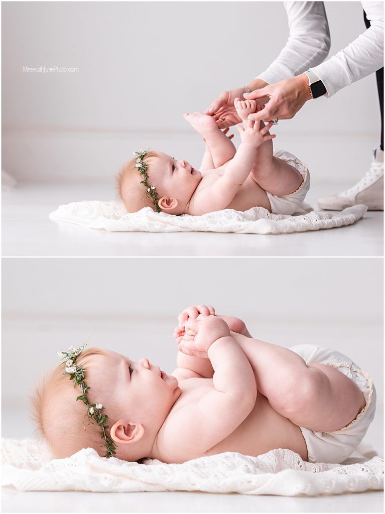Professional newborn photography session showing gentle hands positioning a sleeping baby on soft white fabric.