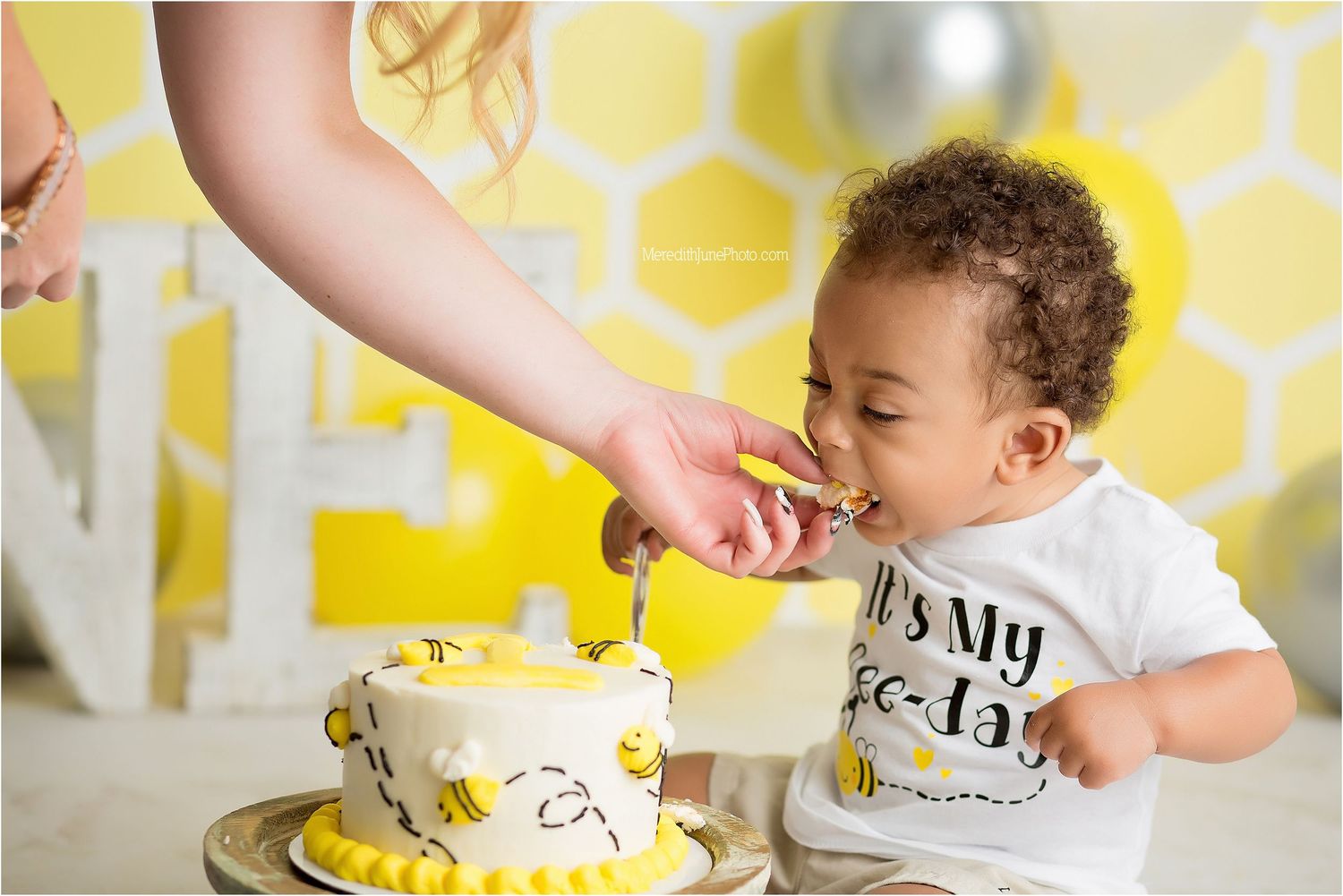 Baby reaching for birthday cake during cake smash photo session with yellow honeycomb pattern background.