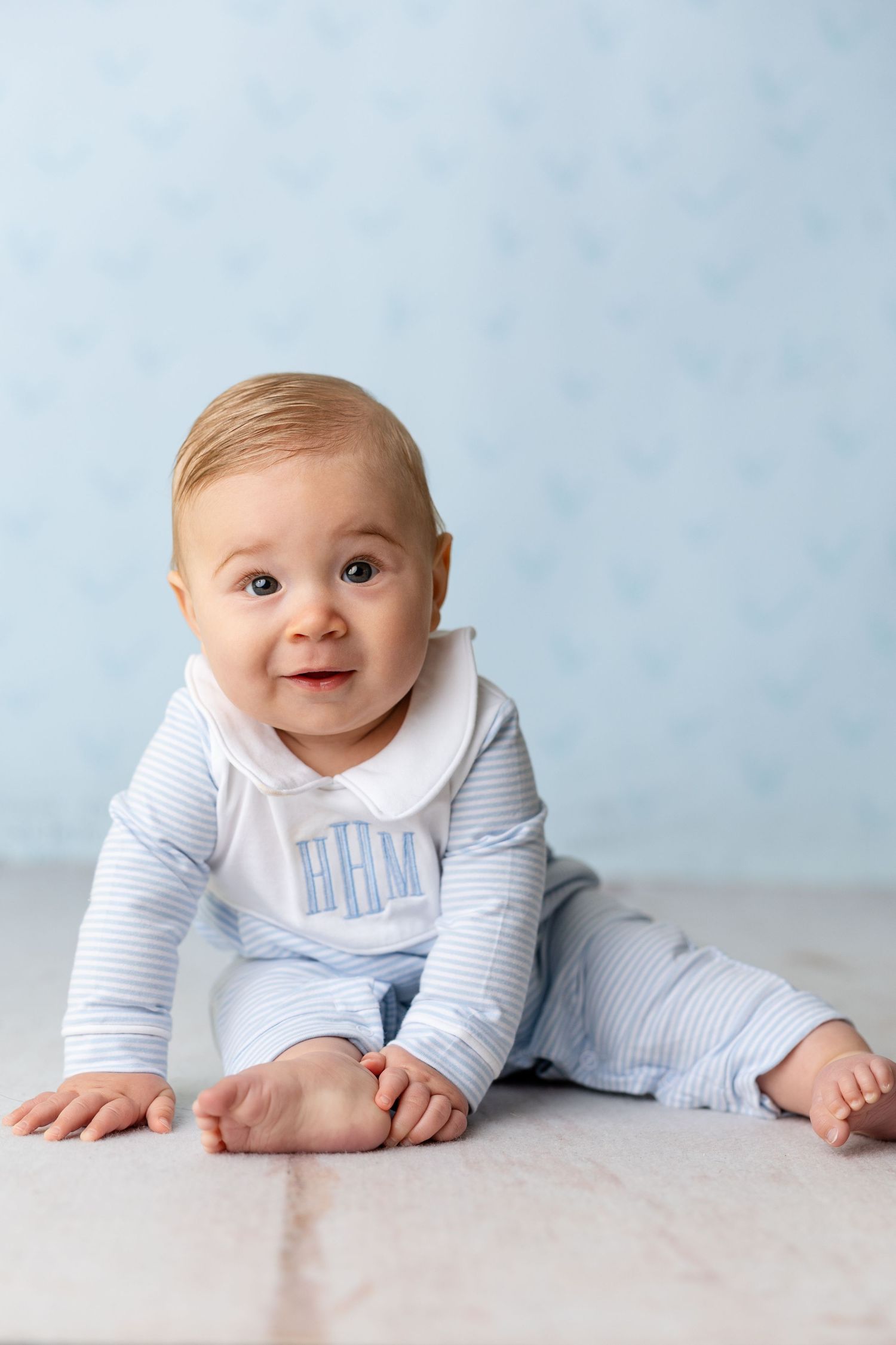 Baby in light blue striped outfit crawls on light gray surface with joyful expression.