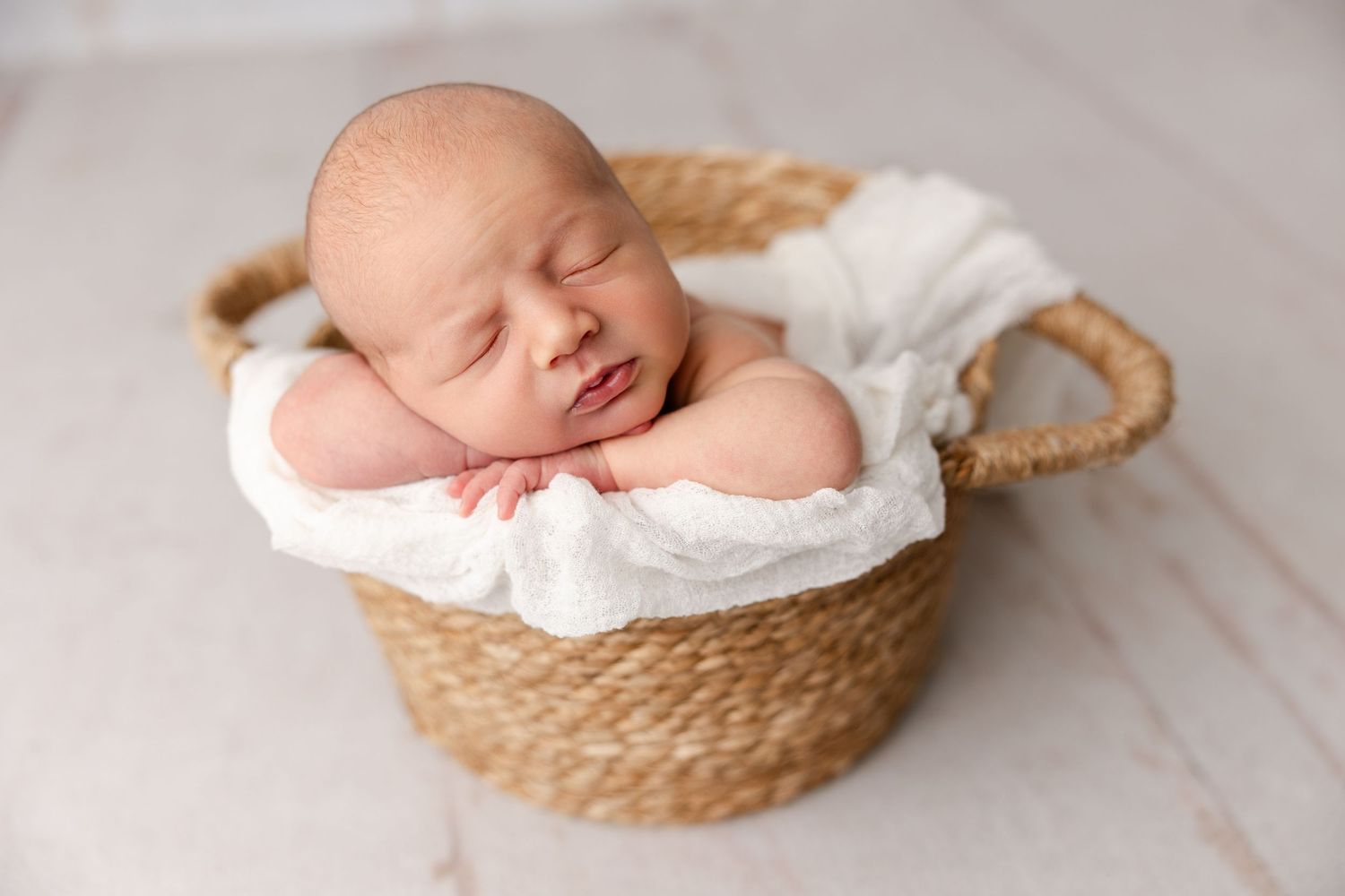 Sleeping newborn baby nestled in woven basket with white wrapping.