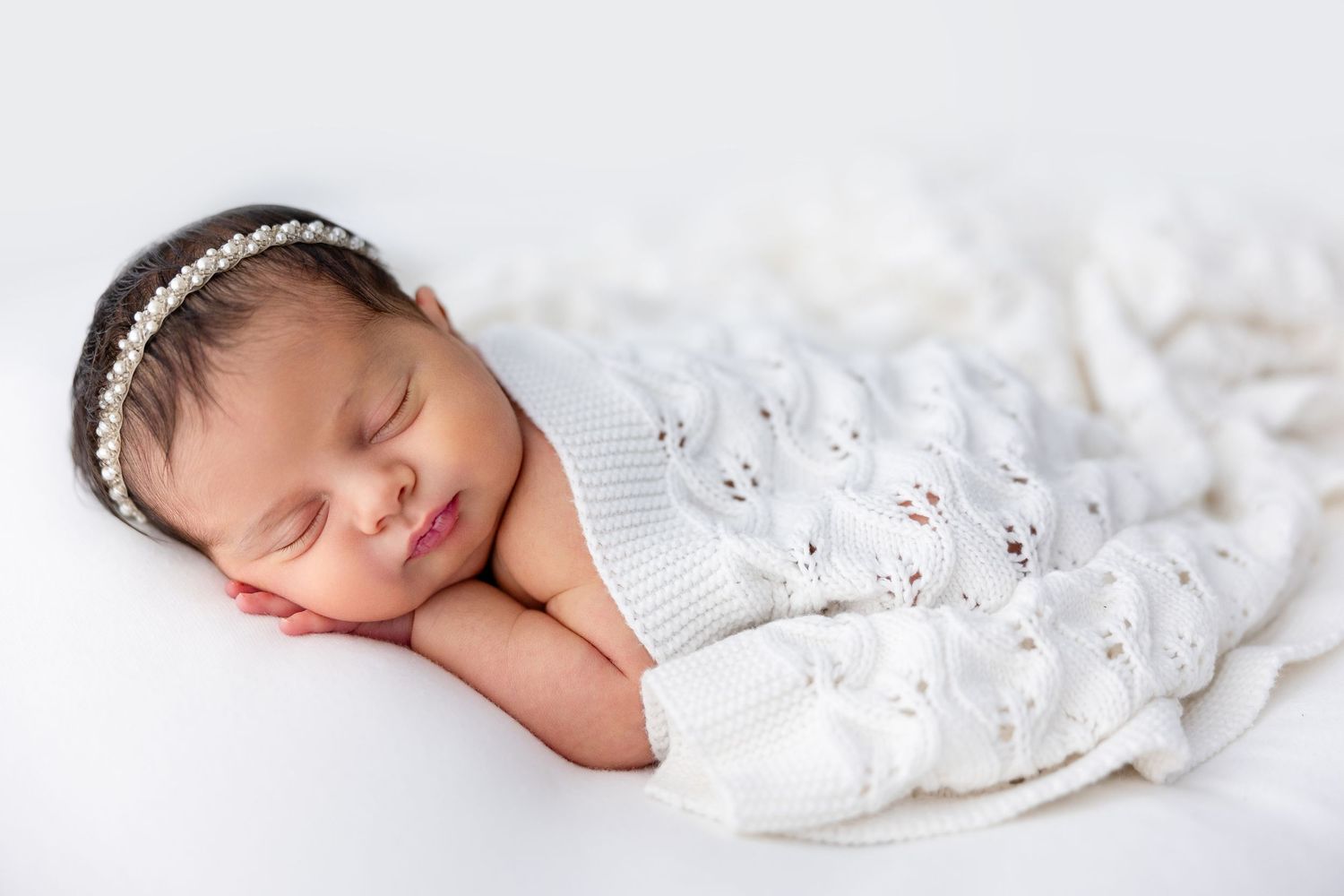 Peaceful newborn baby sleeping in white lace wrap against light background.