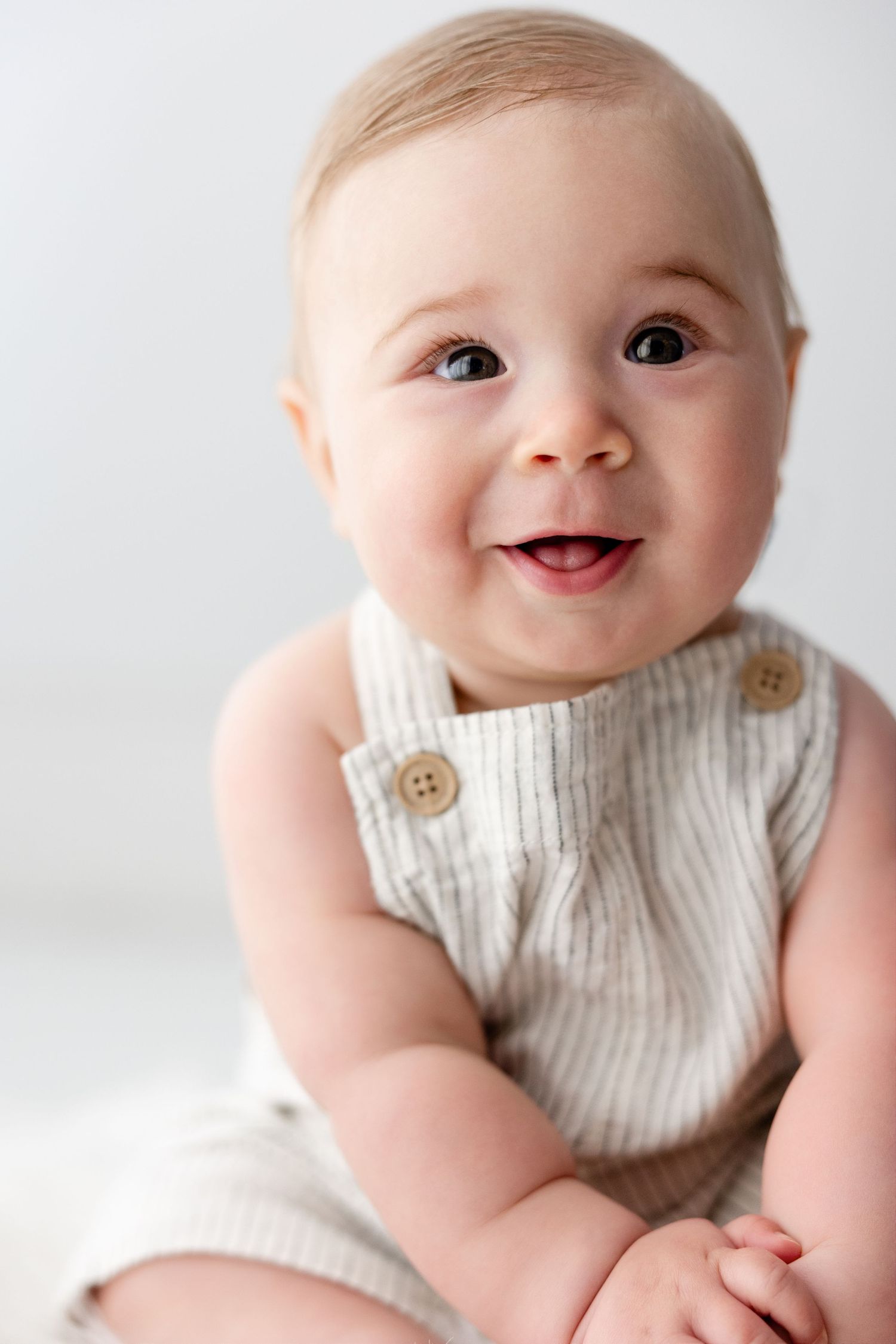 Baby in cream-colored textured outfit smiles brightly against white background.