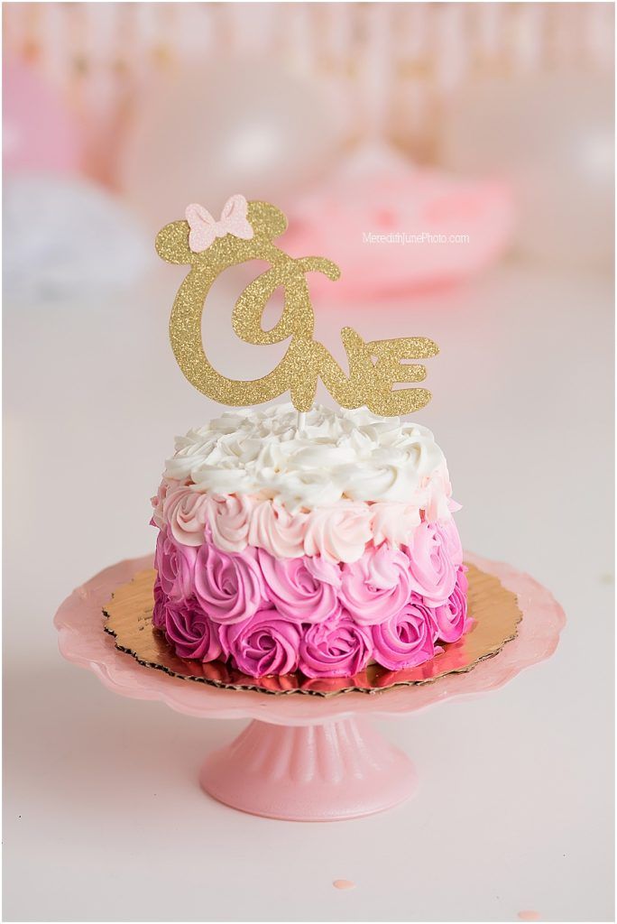 Pink ombre rosette smash cake with gold glitter 'ONE' topper and bow on pink cake stand.