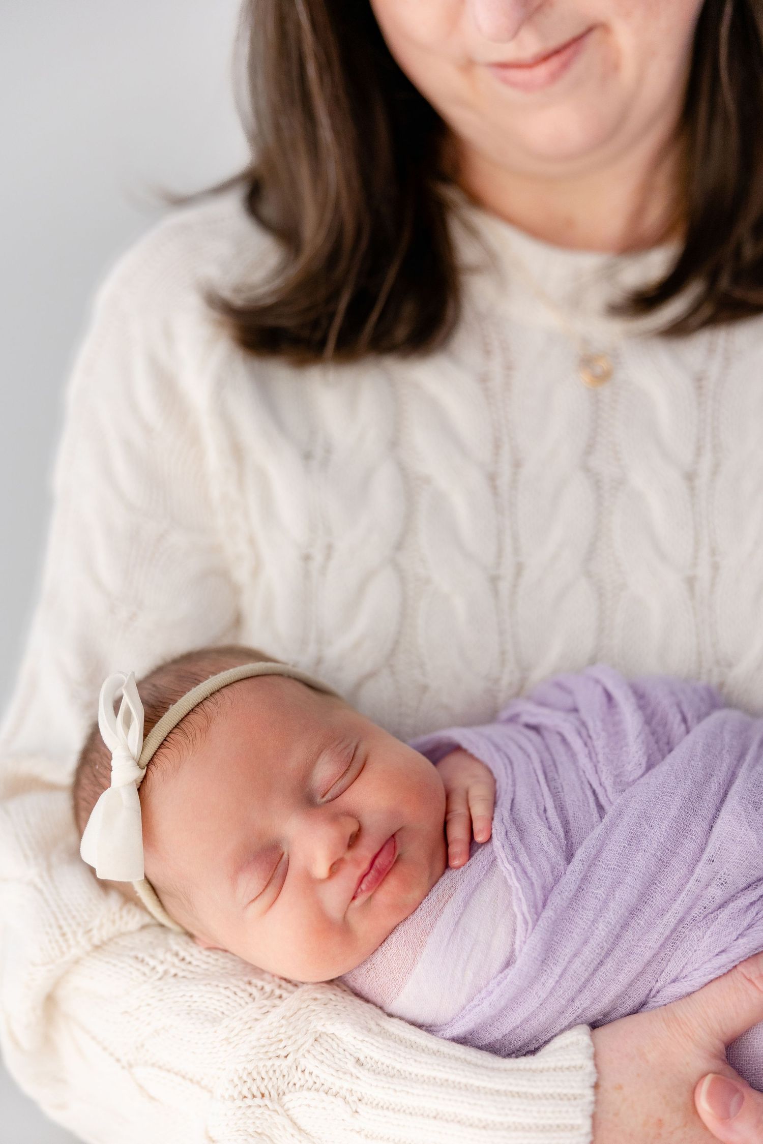 Newborn baby wrapped in purple fabric sleeping peacefully against white background.
