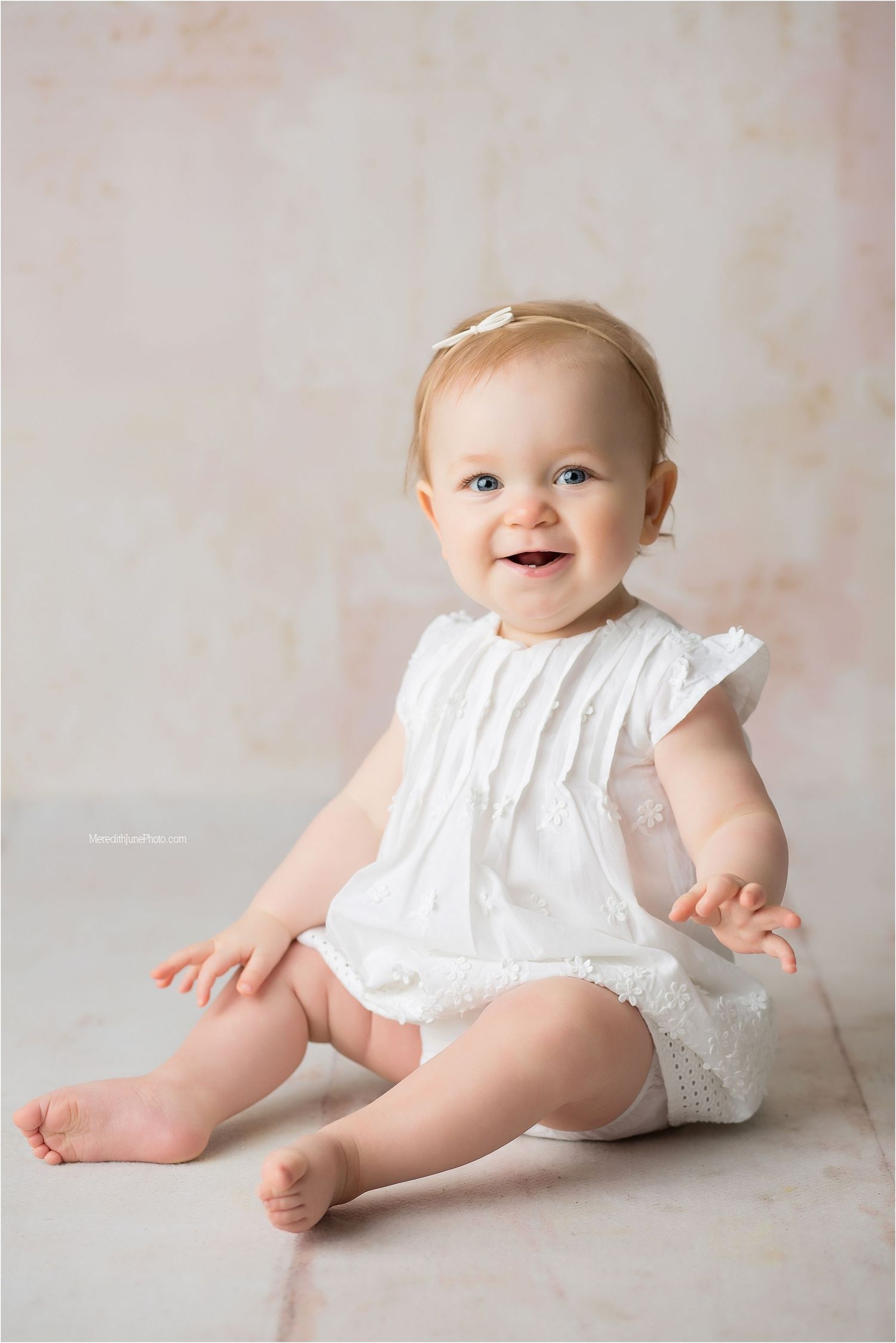 Adorable baby photoshoot featuring white ruffled romper against neutral backdrop.