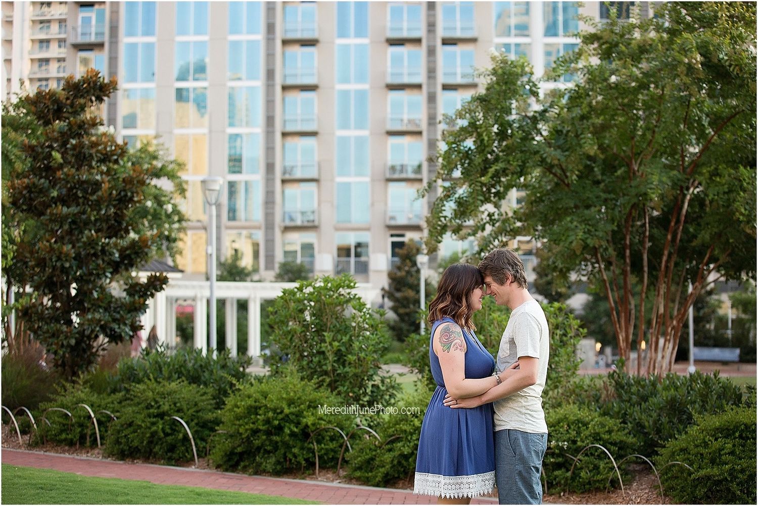 Urban family photoshoot with modern apartment buildings and landscaped gardens in background.