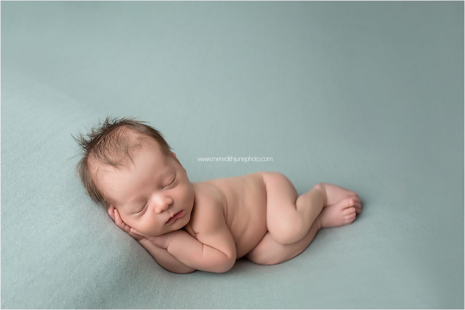 A sleeping newborn baby lies peacefully on soft grey fabric in a minimalist studio setting.