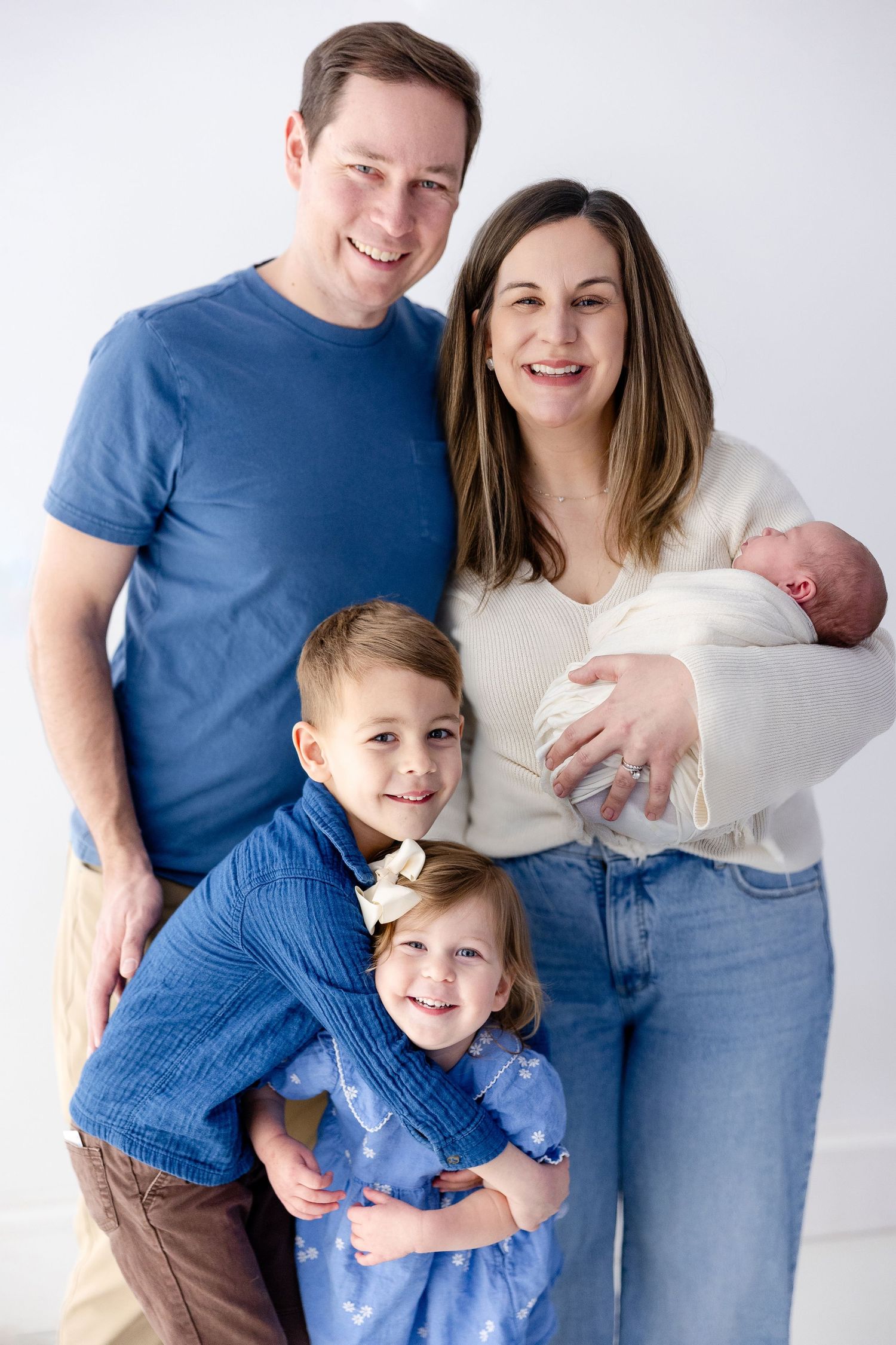 A family of five poses together against a white backdrop wearing coordinating blue and white outfits.