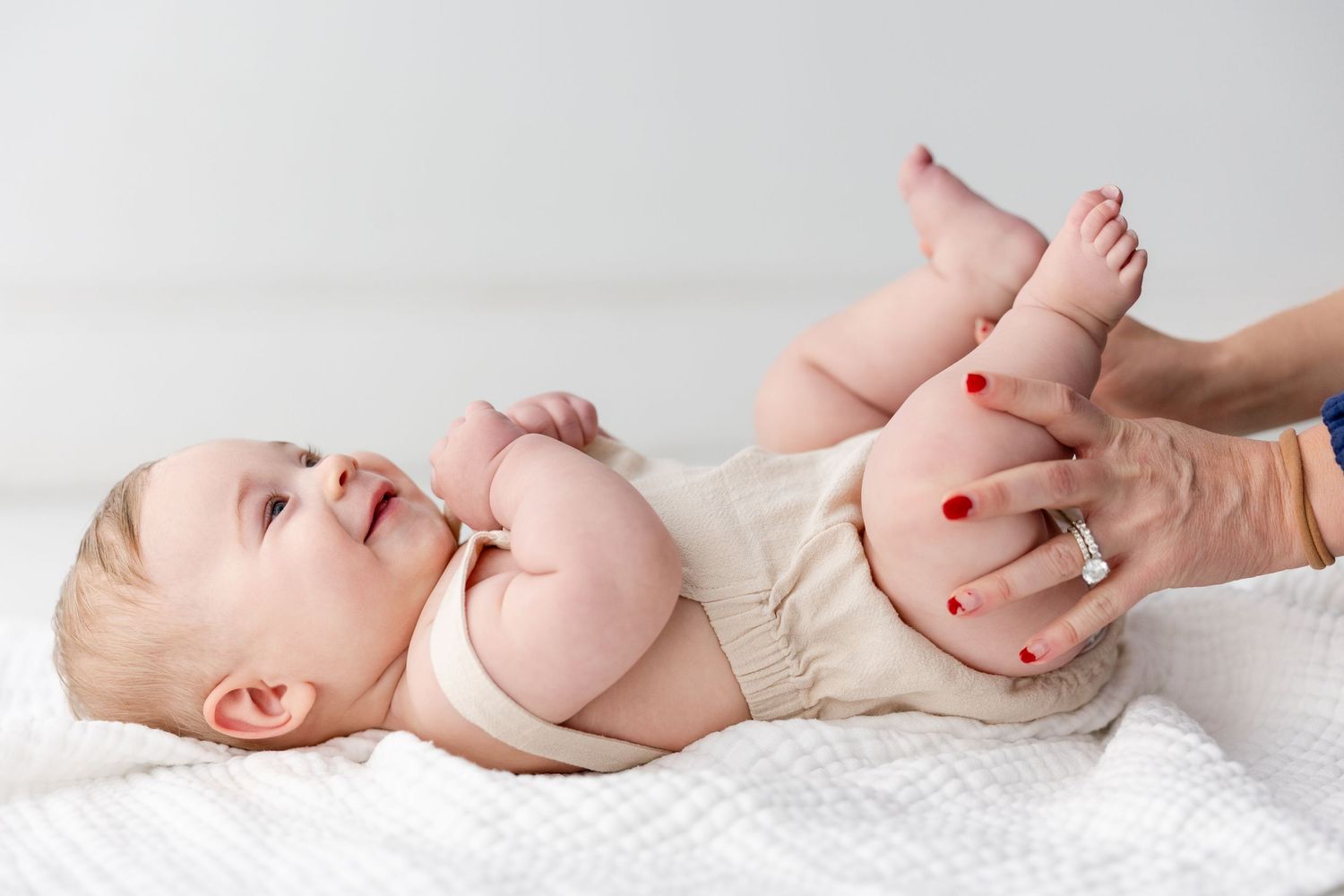A baby lying on white bedding giggles while adult hands change their diaper.