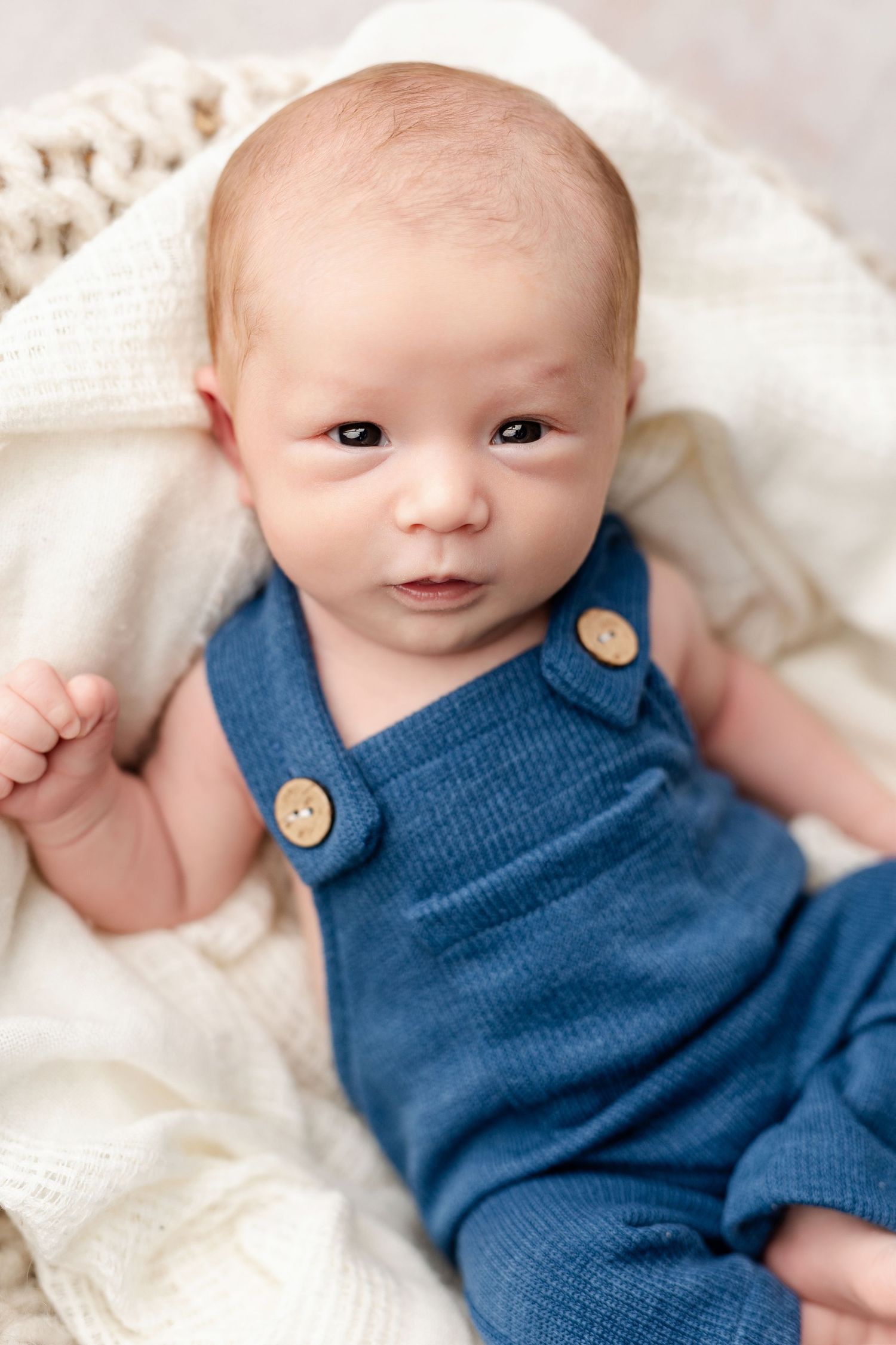 Baby wearing blue knit romper lies on white textured blanket in series of sweet expressions.
