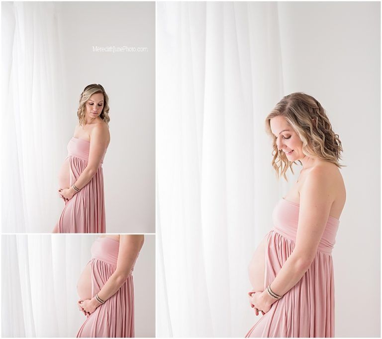A maternity photoshoot featuring a woman in a flowing dusty pink dress against a white backdrop.
