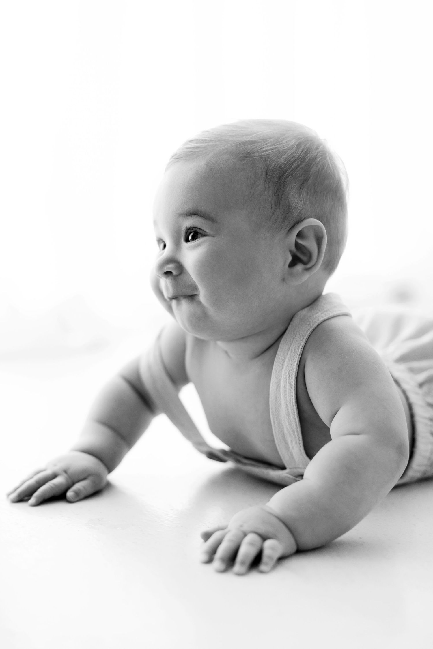 Black and white portrait of an infant in a white tank top lying on their stomach with a gentle smile.