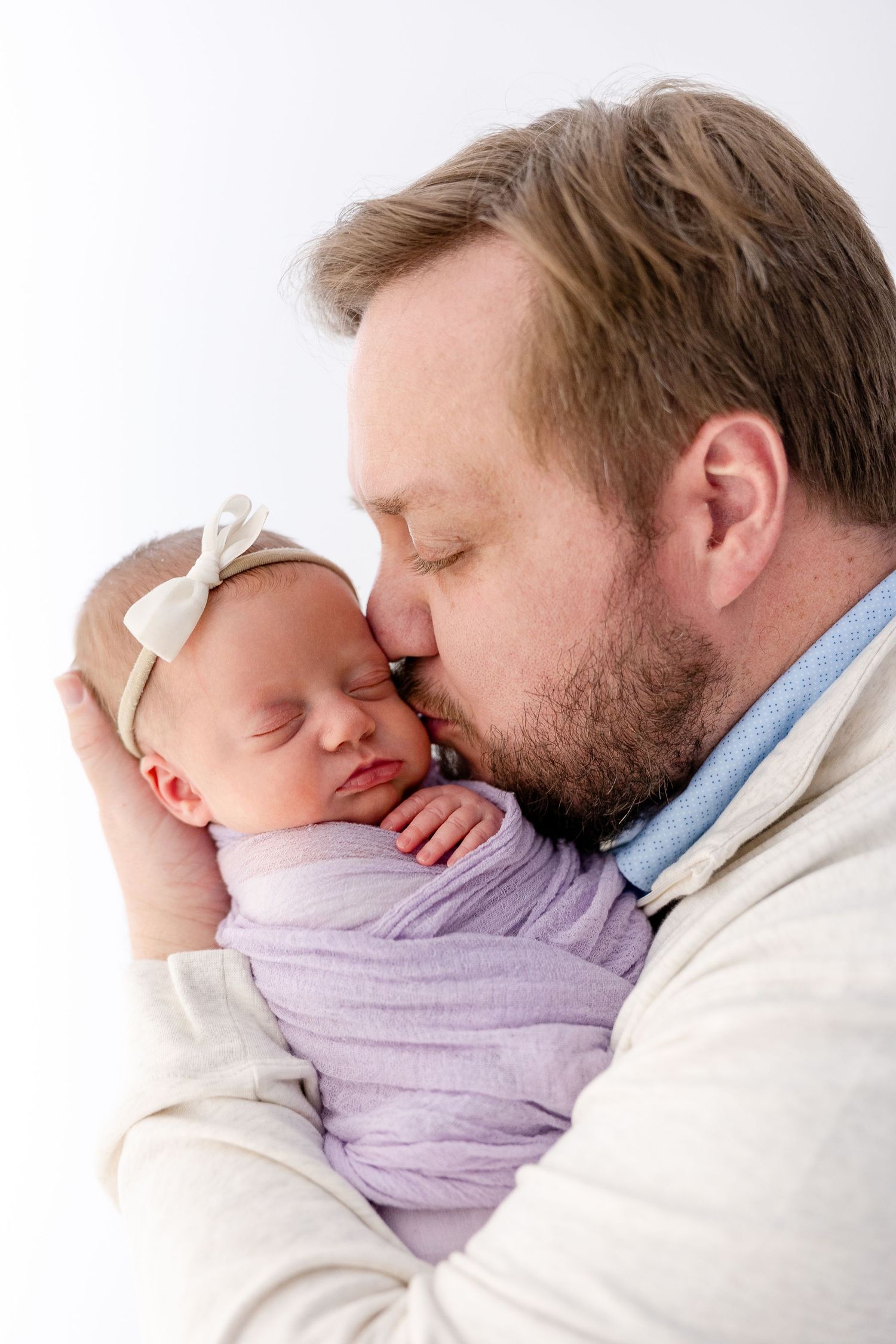 Tender moment between parent and sleeping newborn baby swaddled in purple fabric.