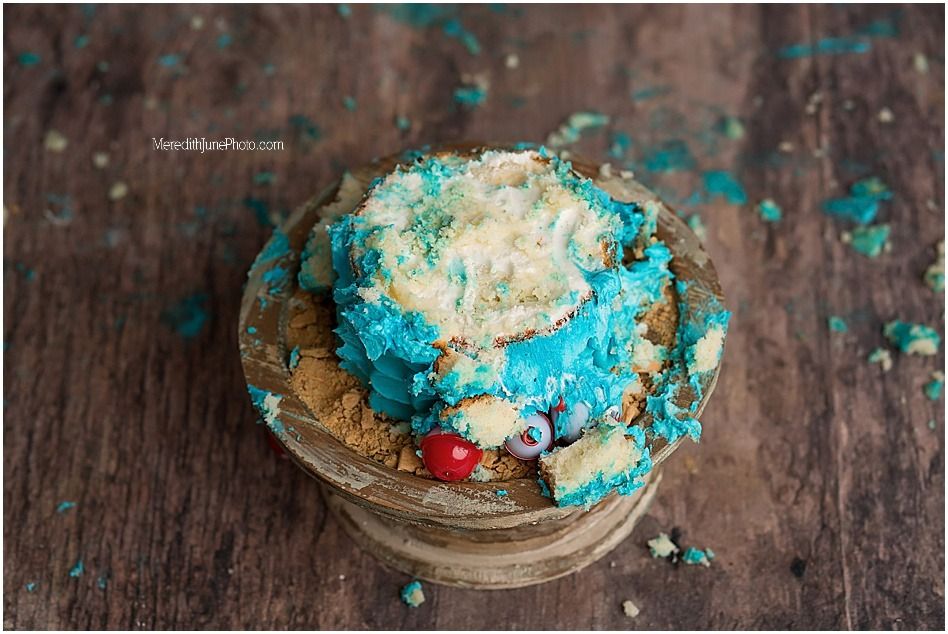 A smashed blue and white birthday cake on a rustic wooden surface with scattered crumbs and frosting.