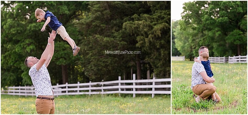 Playful outdoor scene with child being lifted high in the air near white picket fence in grassy field.