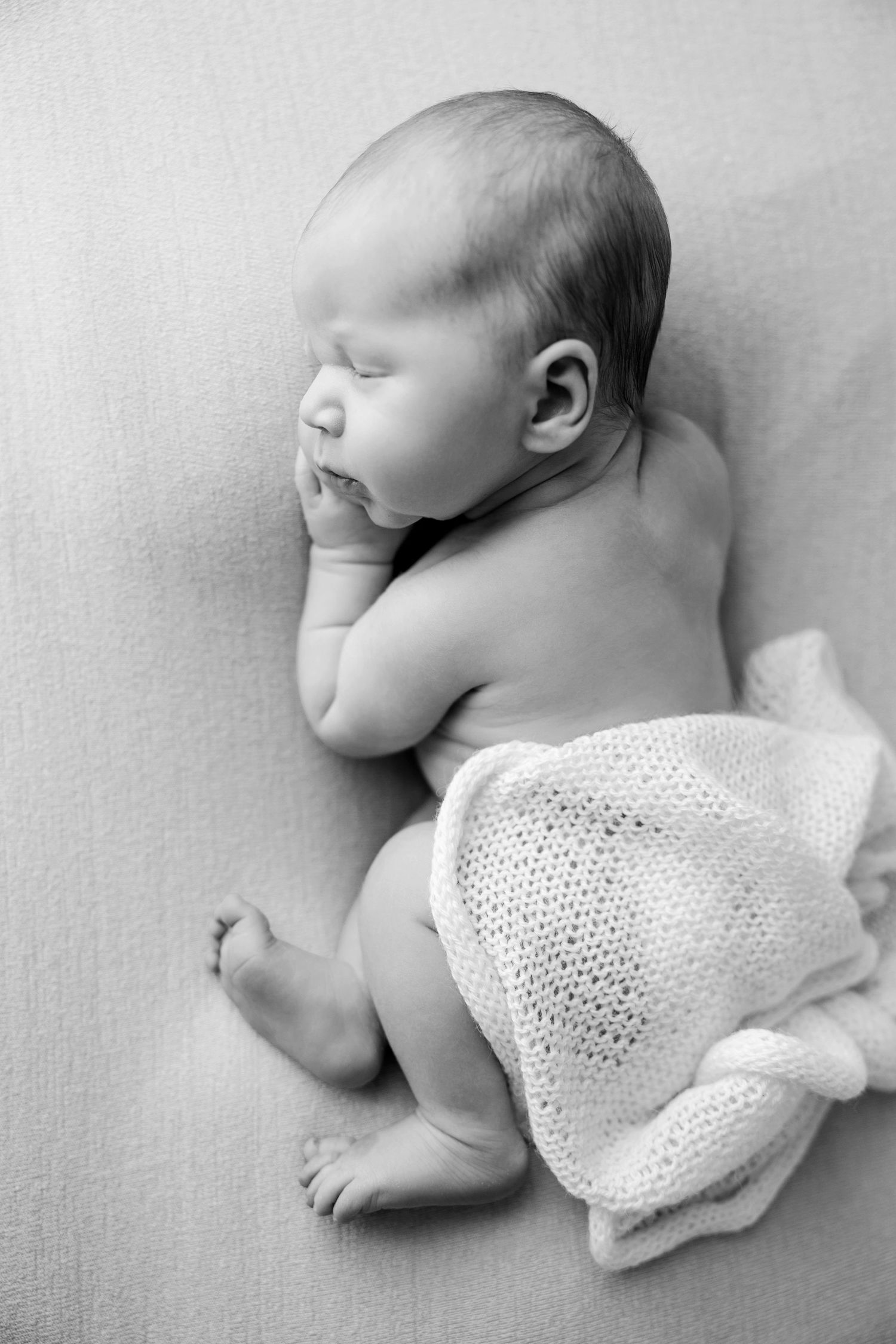 A sleeping newborn baby in white knit wrap lies peacefully on a soft gray background in a series of gentle poses.