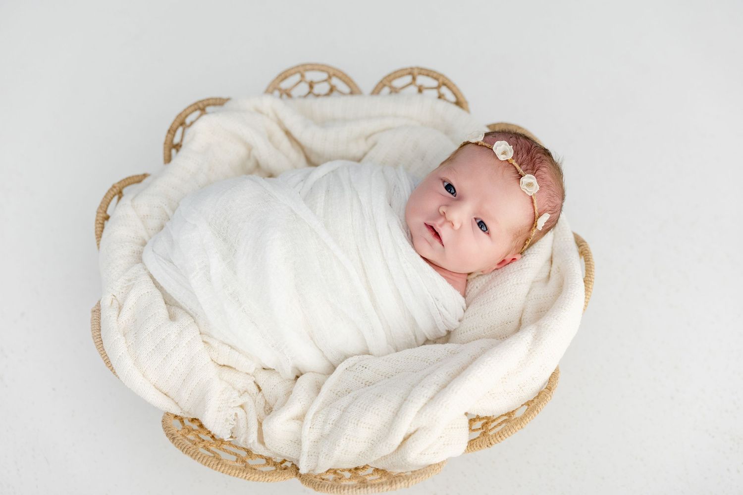 A newborn baby wrapped in white swaddle blankets lies in various poses on neutral backgrounds.