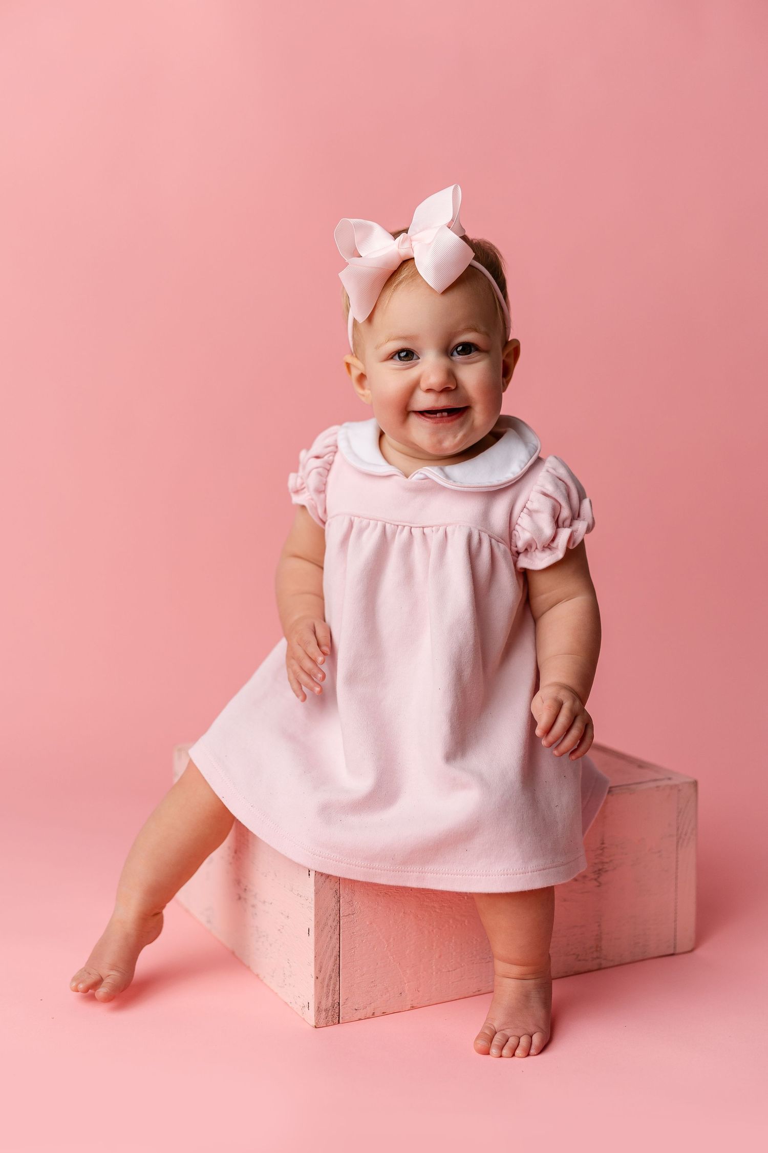 Baby in pink dress sits on wooden box against pink backdrop showing different poses and expressions.