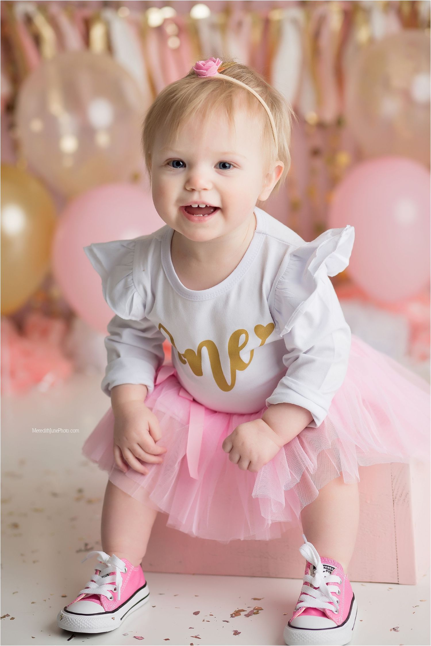 Baby wearing pink tutu and white shirt with gold text crawls and plays on pink backdrop with sparkly decorations.