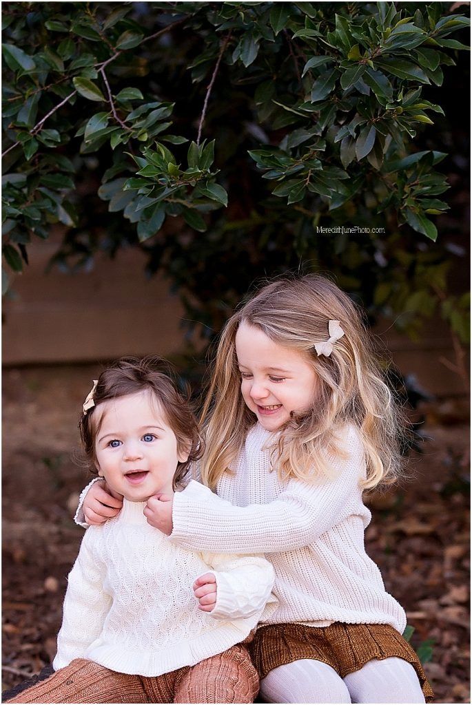 Two children in white sweaters share a sweet moment while sitting together on a bench in an outdoor setting.