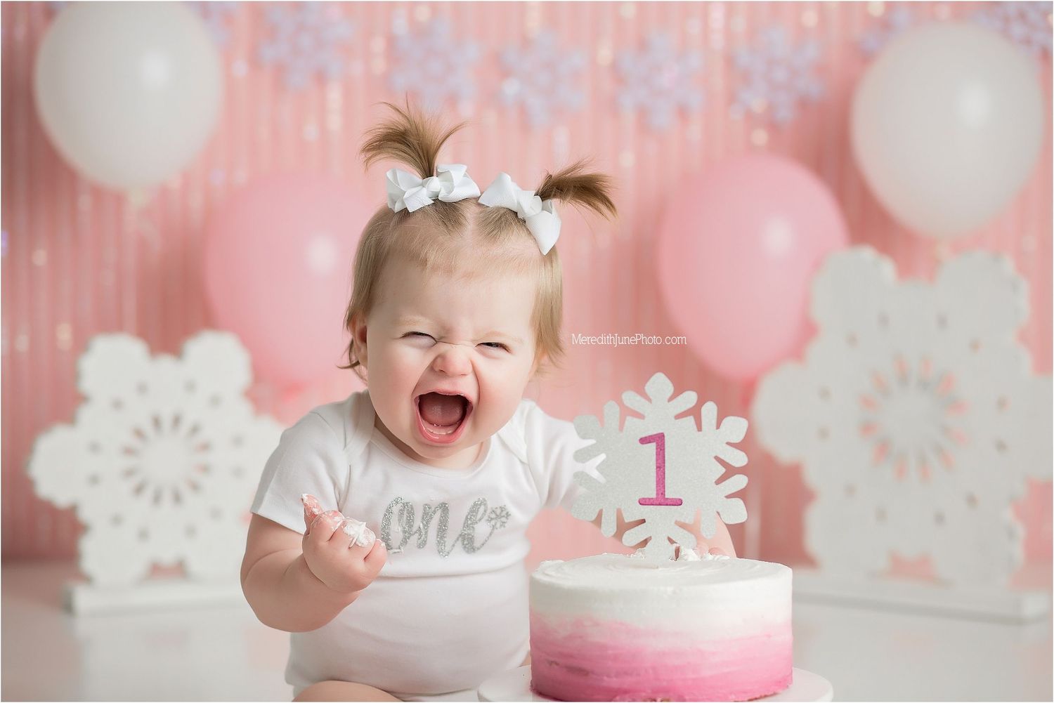 Pink and white winter wonderland themed first birthday party setup with snowflake decorations and balloons.