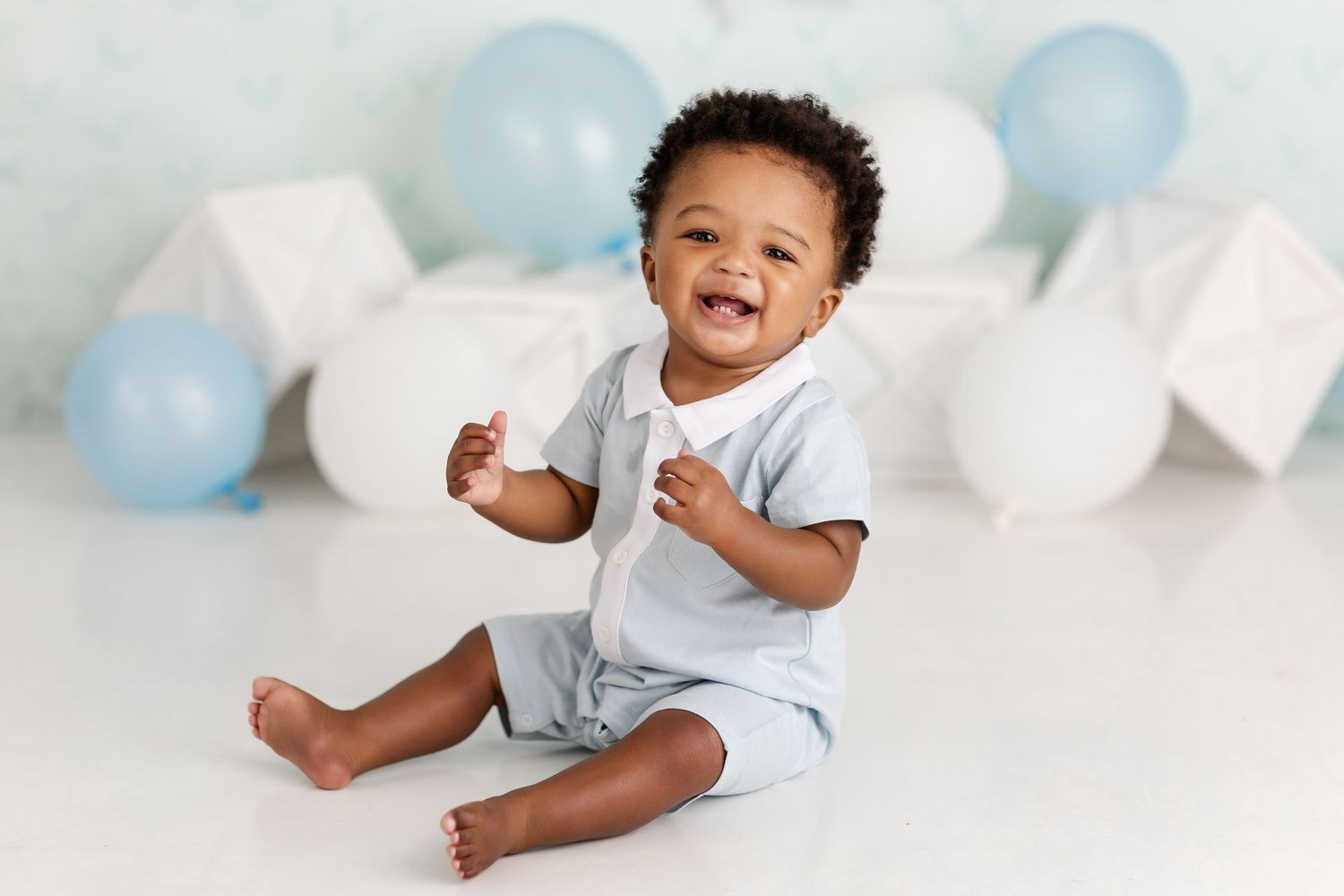 Baby in light blue outfit playing with balloons during photo session.