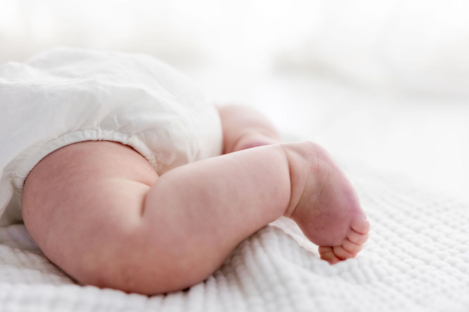 Close up view of tiny newborn baby feet and toes against white blanket background.