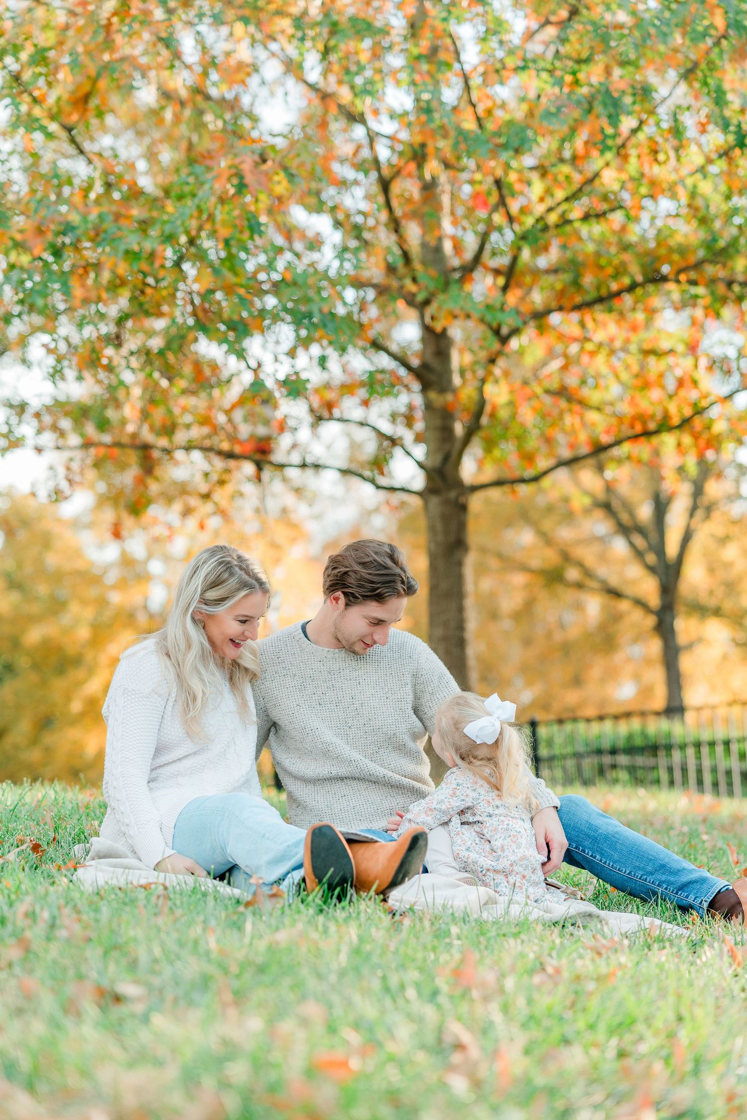 Family lying on grass during autumn photoshoot with golden leaves in background.