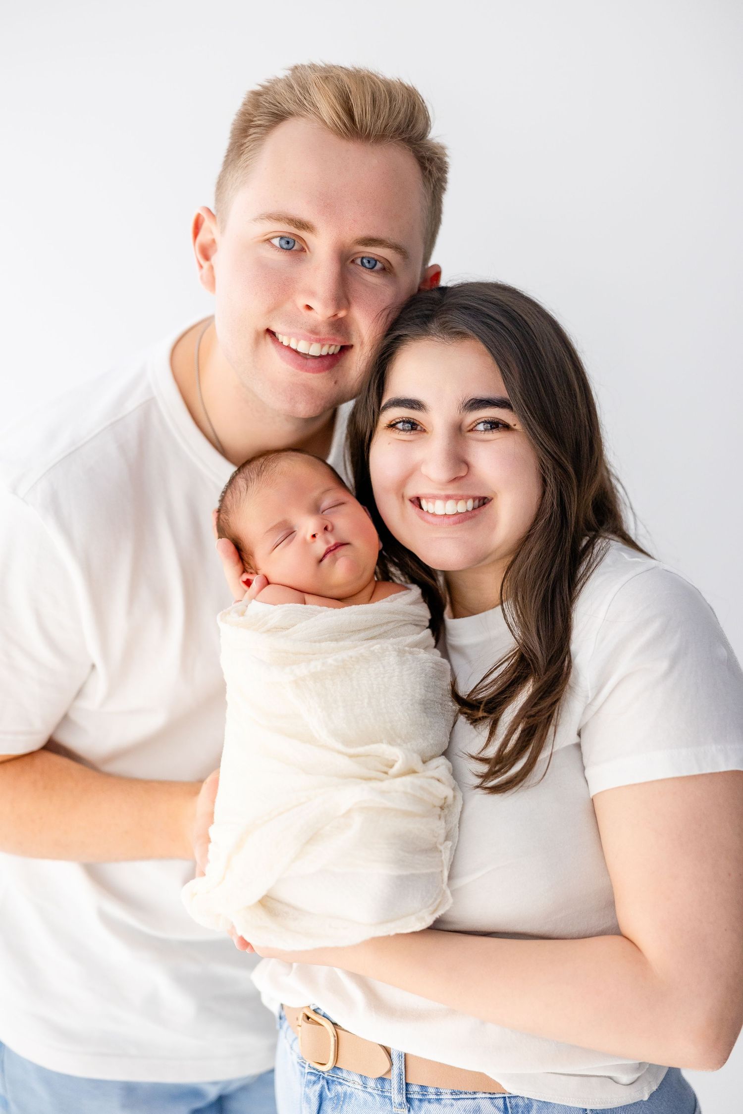 Family portrait with white backdrop showing tender moments in matching white outfits.