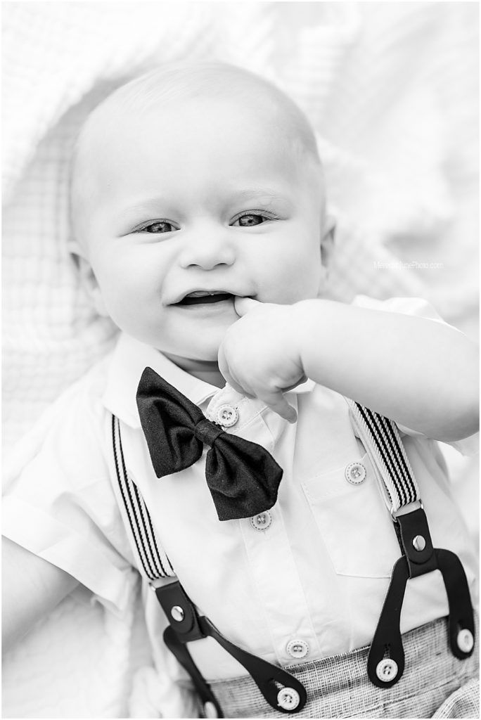 A black and white photo series showing a baby in formal attire with suspenders and bow tie smiling at the camera.