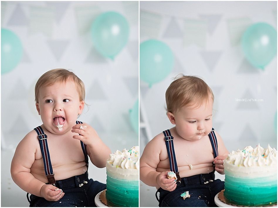 Baby in navy overalls enjoying first birthday cake smash with teal decorations.