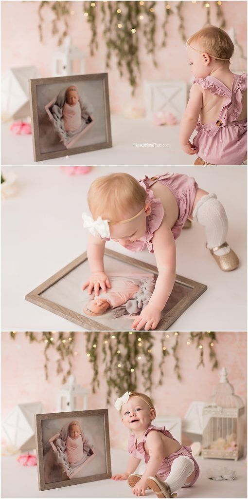 Baby in pink dress plays with vintage mirror on pink backdrop with hanging floral decorations.